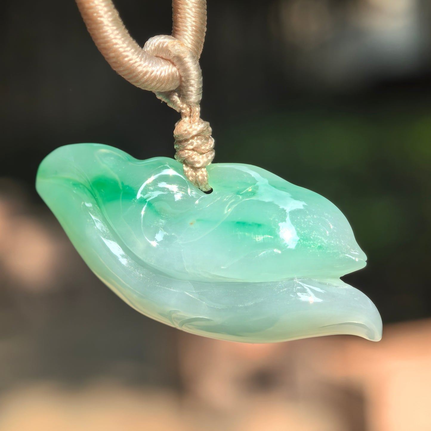Natural Grade-A glutinous floating green dolphin jadeite pendant hanging with cord, showing a three-dimensional wave-riding dolphin design.