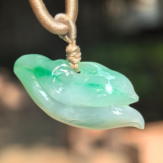 Natural Grade-A glutinous floating green dolphin jadeite pendant hanging with cord, showing a three-dimensional wave-riding dolphin design.
