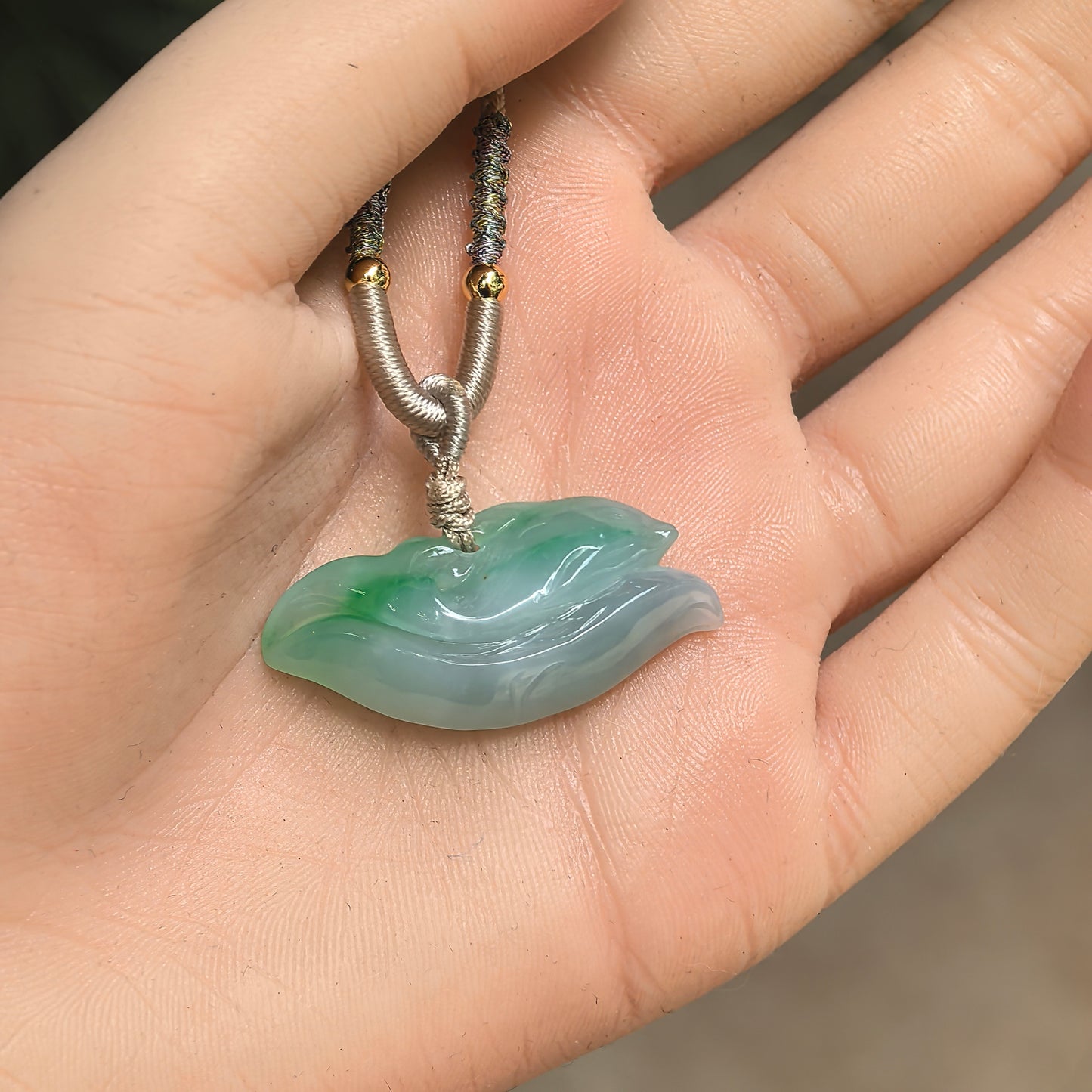 Natural Grade-A green dolphin jadeite pendant shown in hand, displaying its compact size and soft translucent glutinous texture.