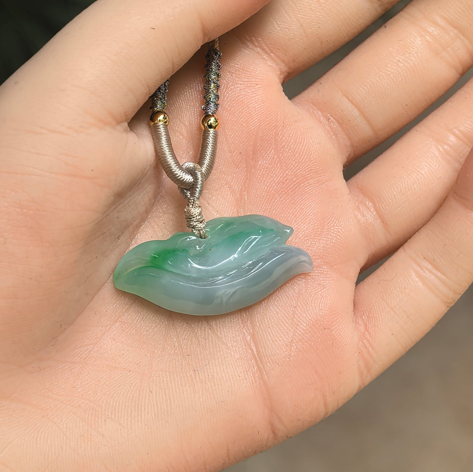 Natural Grade-A green dolphin jadeite pendant shown in hand, displaying its compact size and soft translucent glutinous texture.