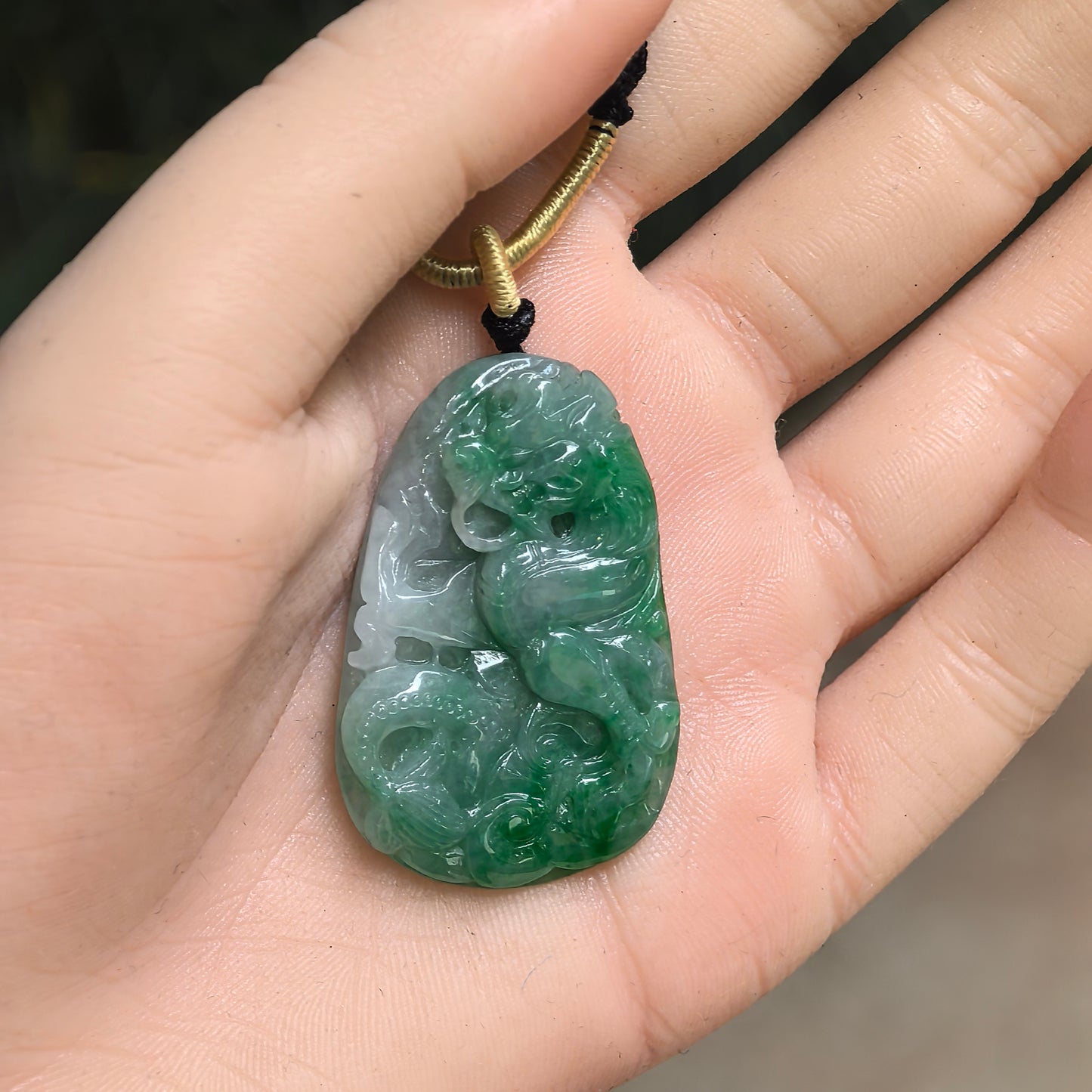 Natural Grade-A glutinous green dragon plaque jadeite pendant shown in hand with raised carved dragon details.