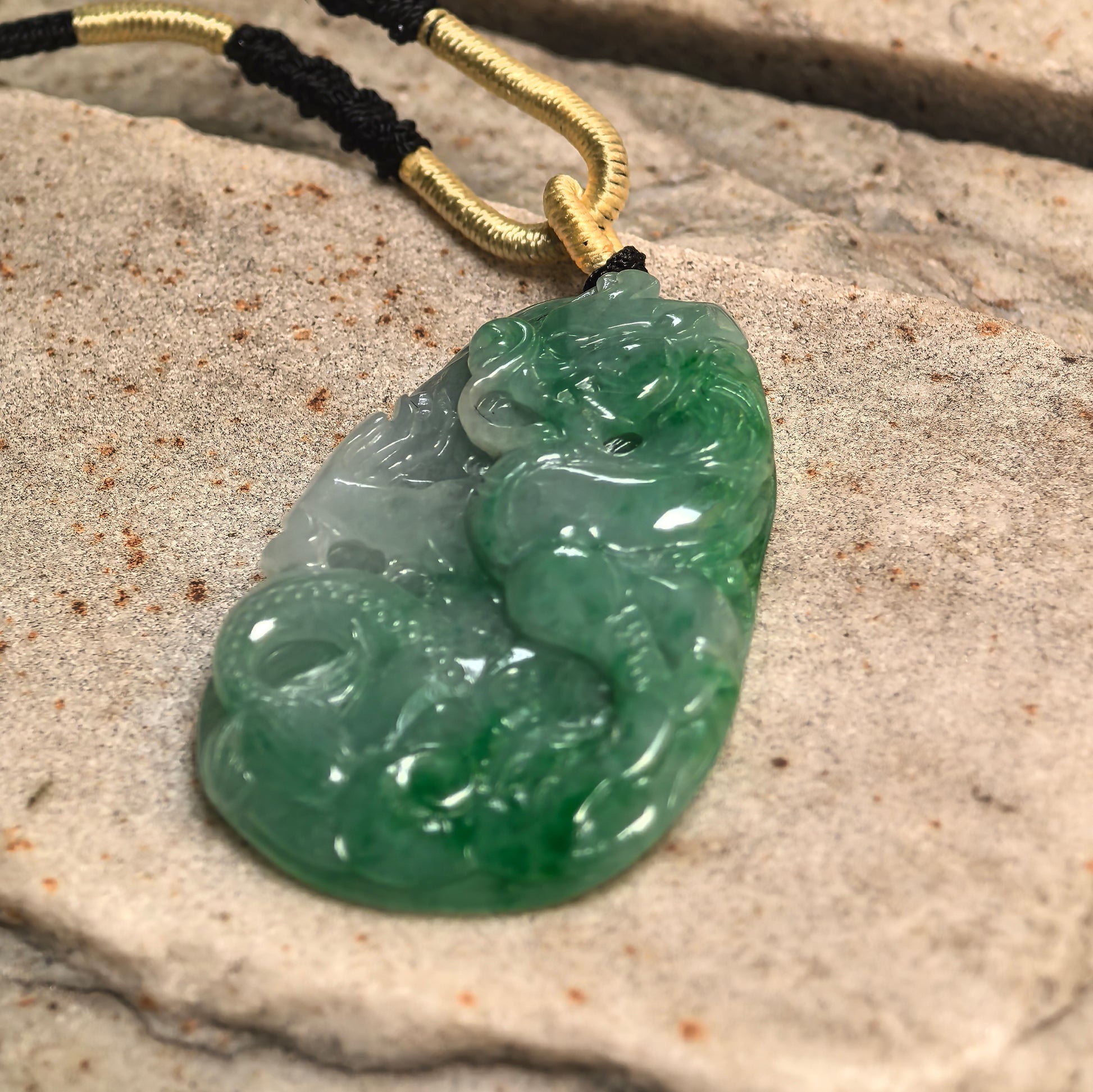 Side view of glutinous green jadeite dragon plaque pendant on stone surface showing raised carving and polished finish.