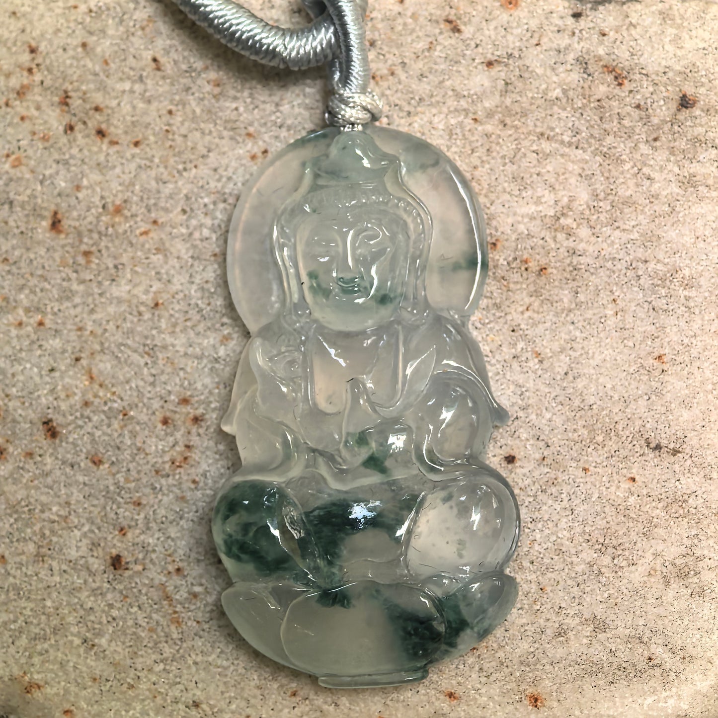 Close-up of Guanyin jadeite pendant showing calm facial carving and natural green inclusions.
