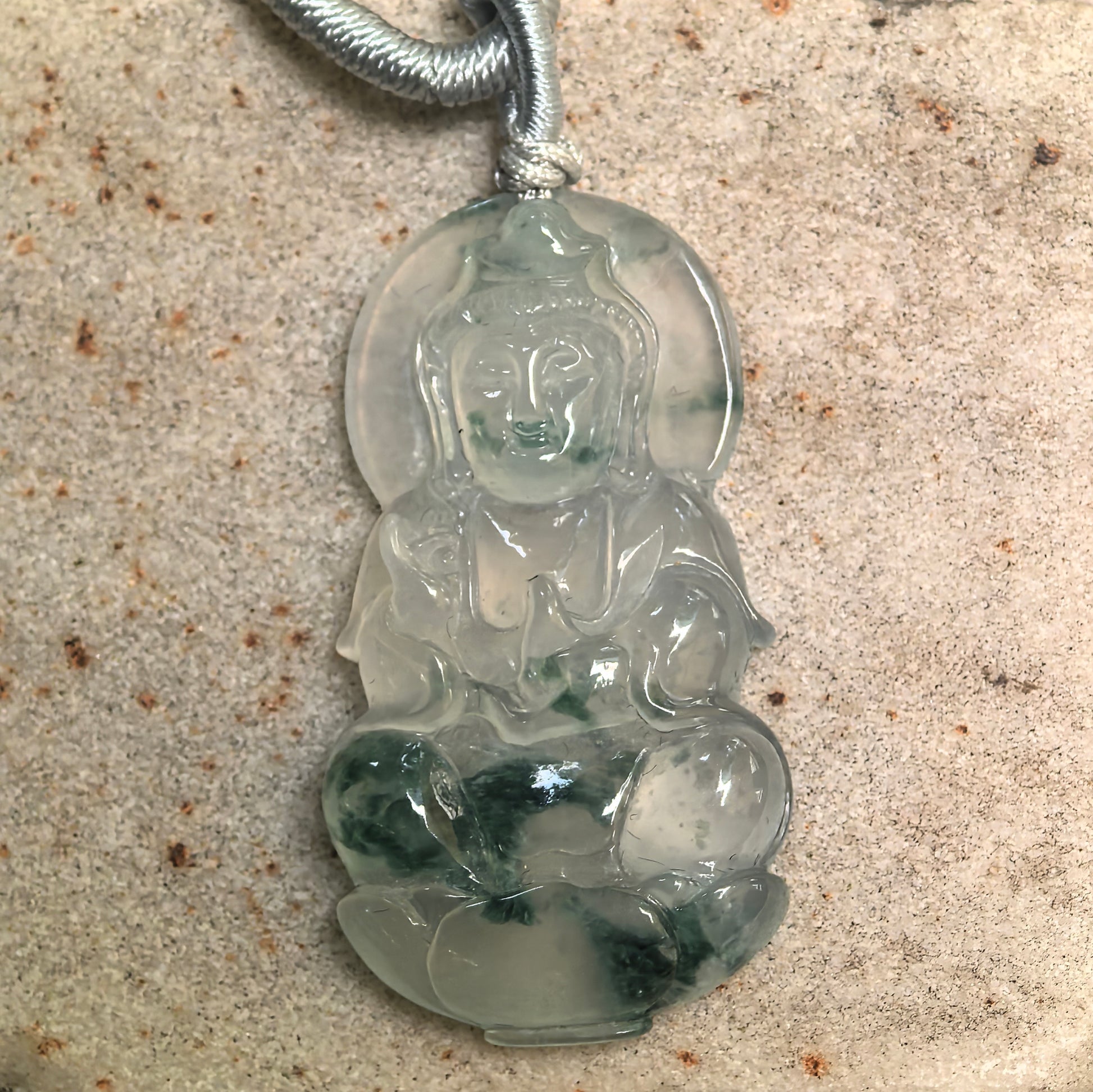 Close-up of Guanyin jadeite pendant showing calm facial carving and natural green inclusions.
