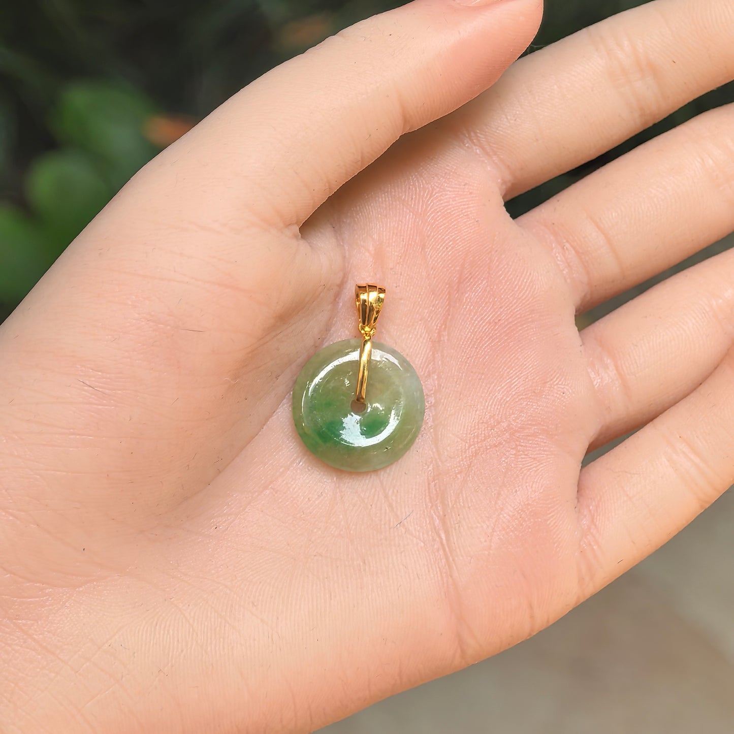 Natural Grade-A icy glutinous yellow-green Peace jadeite pendant with 18K gold bail shown in hand.