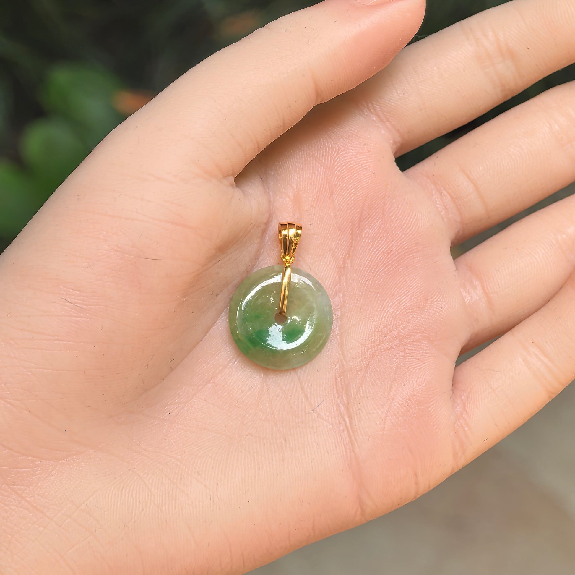 Natural Grade-A icy glutinous yellow-green Peace jadeite pendant with 18K gold bail shown in hand.
