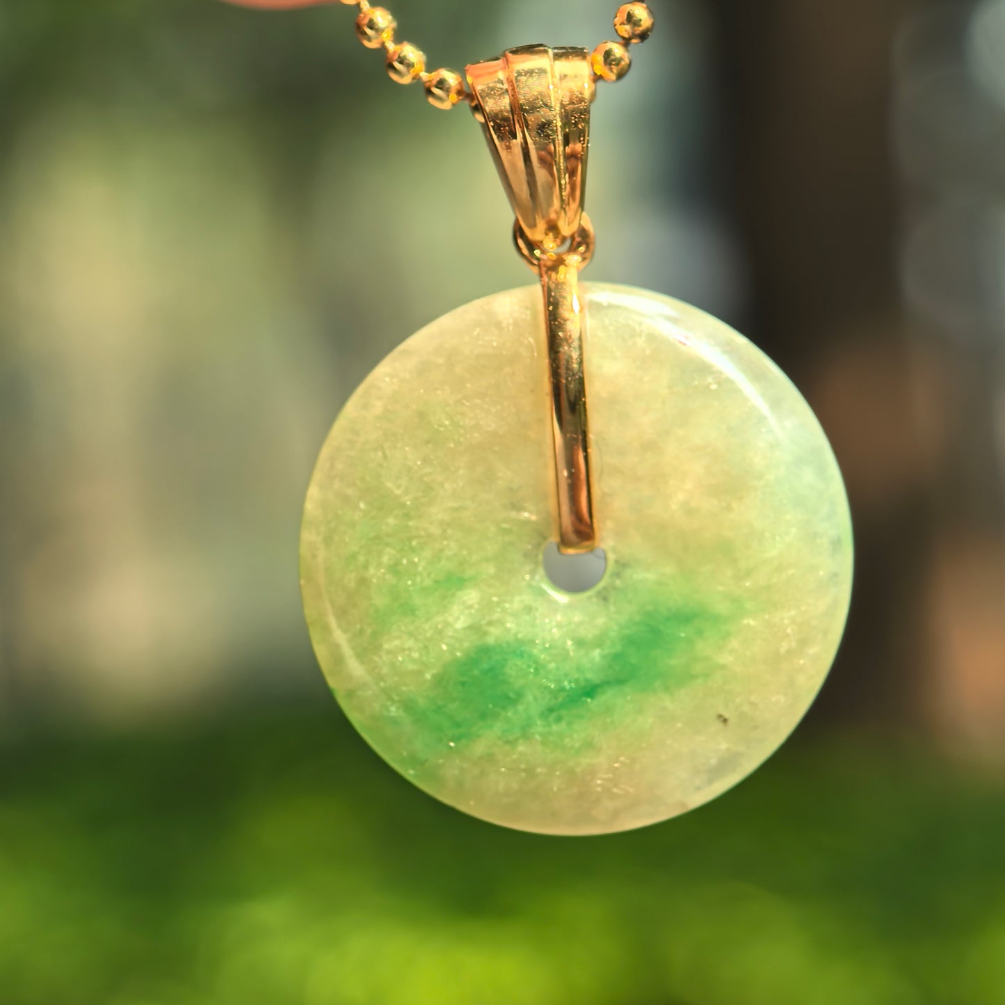 Close-up of yellow-green round Peace jadeite pendant with deeper green floating accent and gold bail.