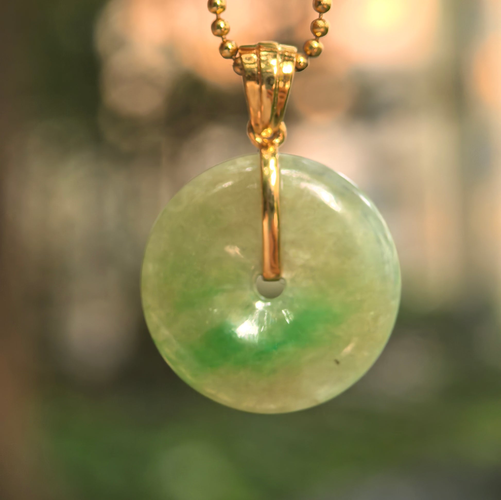 Natural Grade-A yellow-green Peace jadeite pendant hanging under soft light with glossy surface.