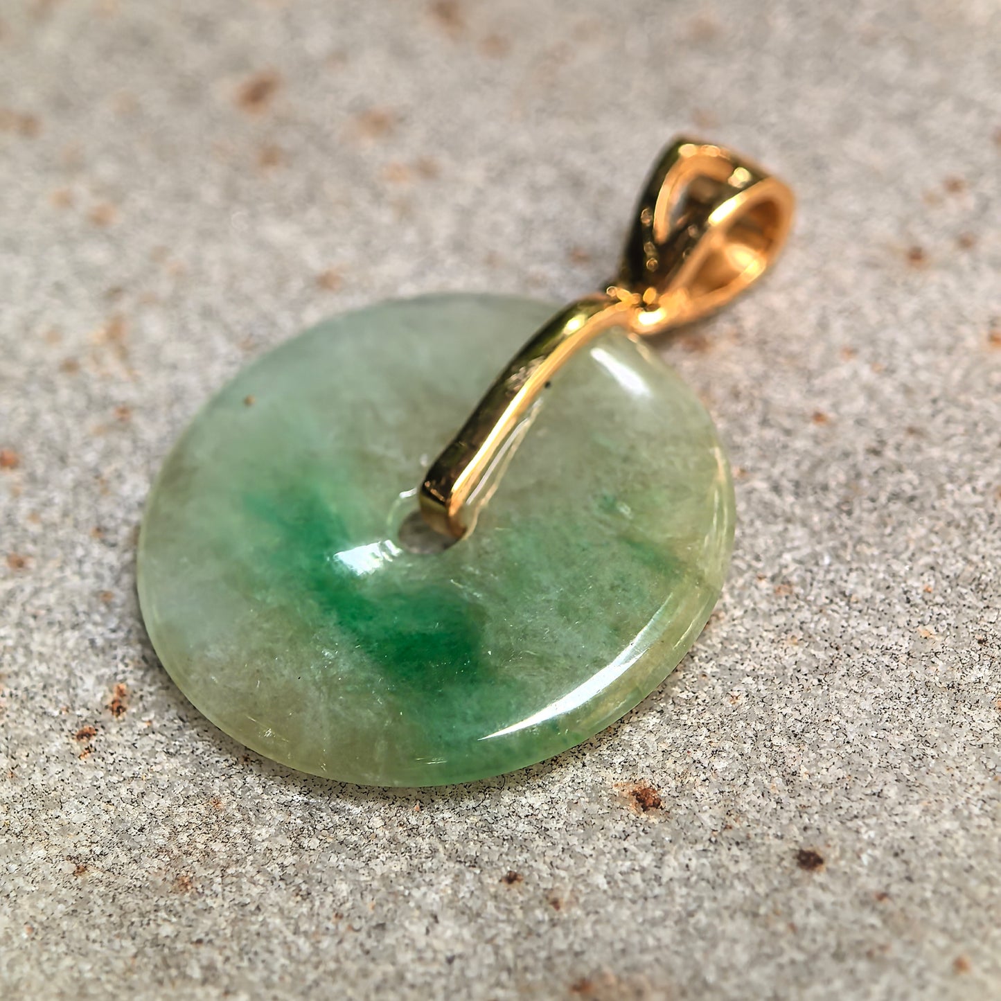 Round icy glutinous jadeite Peace Pendant shown on stone background with 18K gold bail.