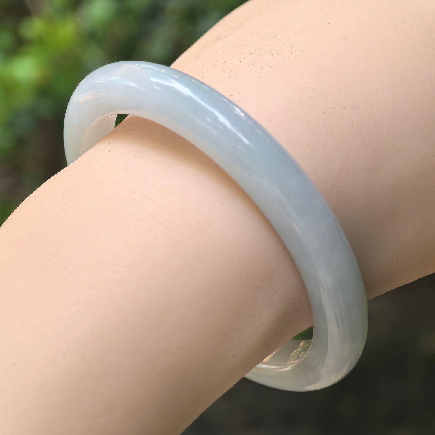 Natural Grade-A glutinous light green D-shape jadeite bangle worn on wrist.