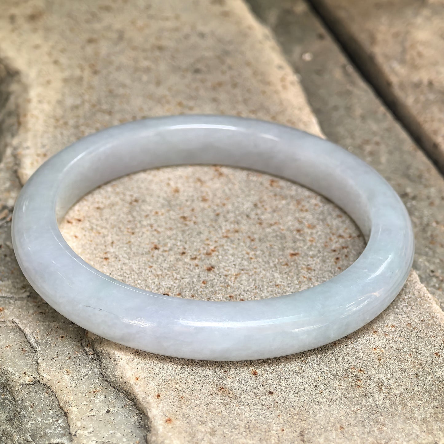 Natural light green jadeite D-shape bangle with slim profile and glossy polished surface.