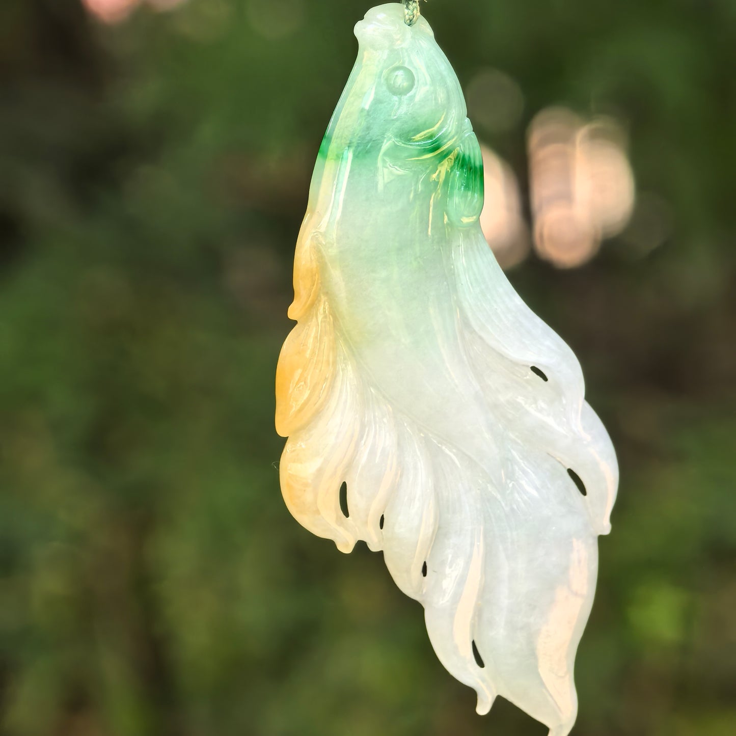 Close-up of yellow-green jadeite fish pendant showing vivid carved details.