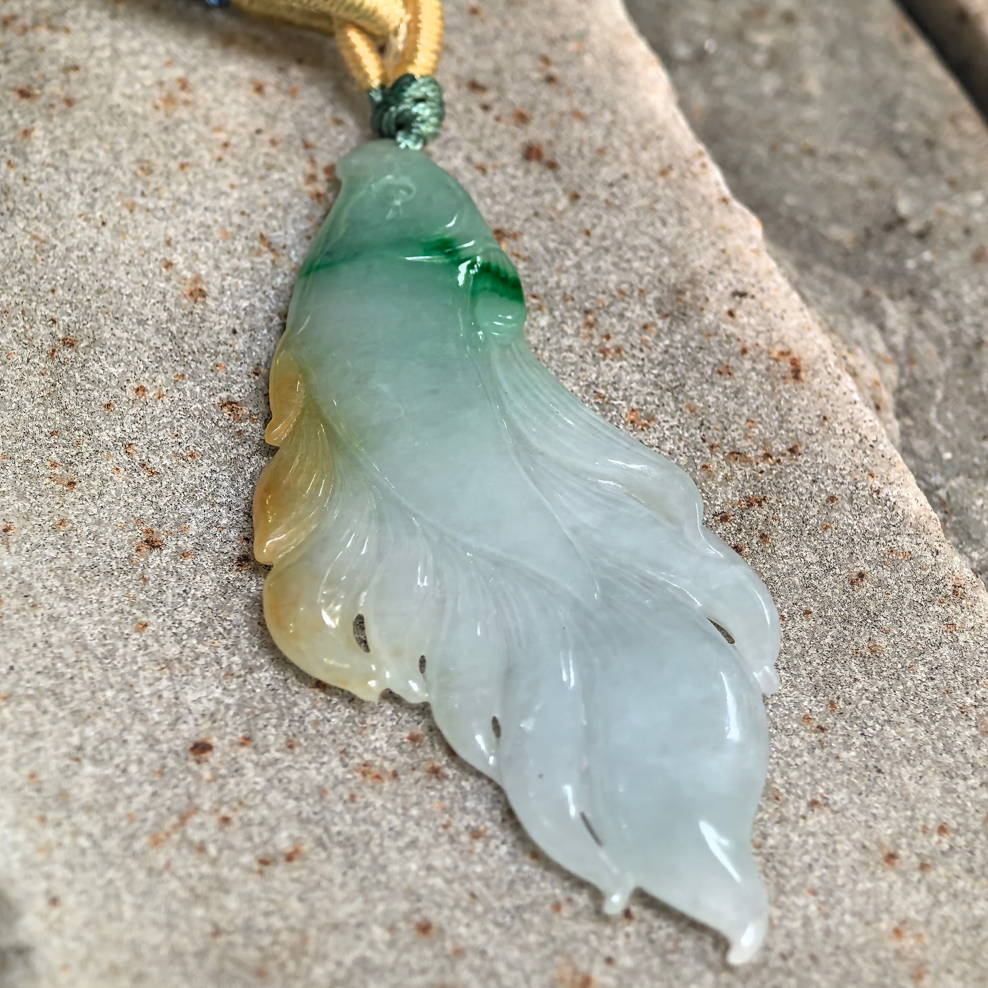 Glutinous yellow-green jadeite fish pendant displayed on stone background.