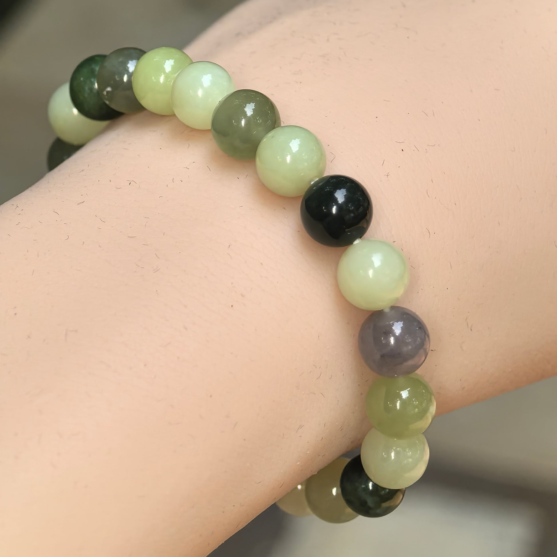 Natural multicolor Hetian jade bead bracelet worn on the wrist with yellow-green, dark green, white, gray, and brown beads.

