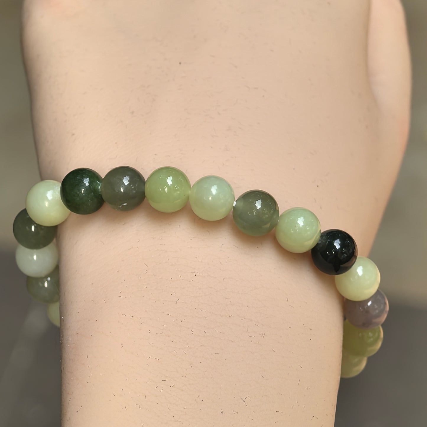 Close-up of round multicolor Hetian jade beads showing smooth polished luster on the wrist.

