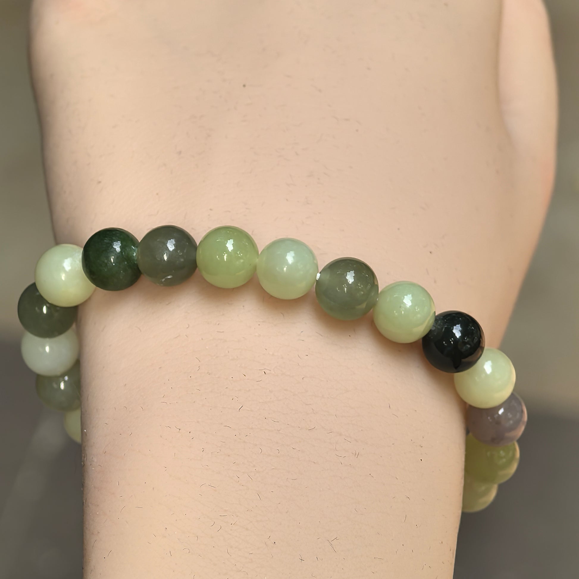 Close-up of round multicolor Hetian jade beads showing smooth polished luster on the wrist.
