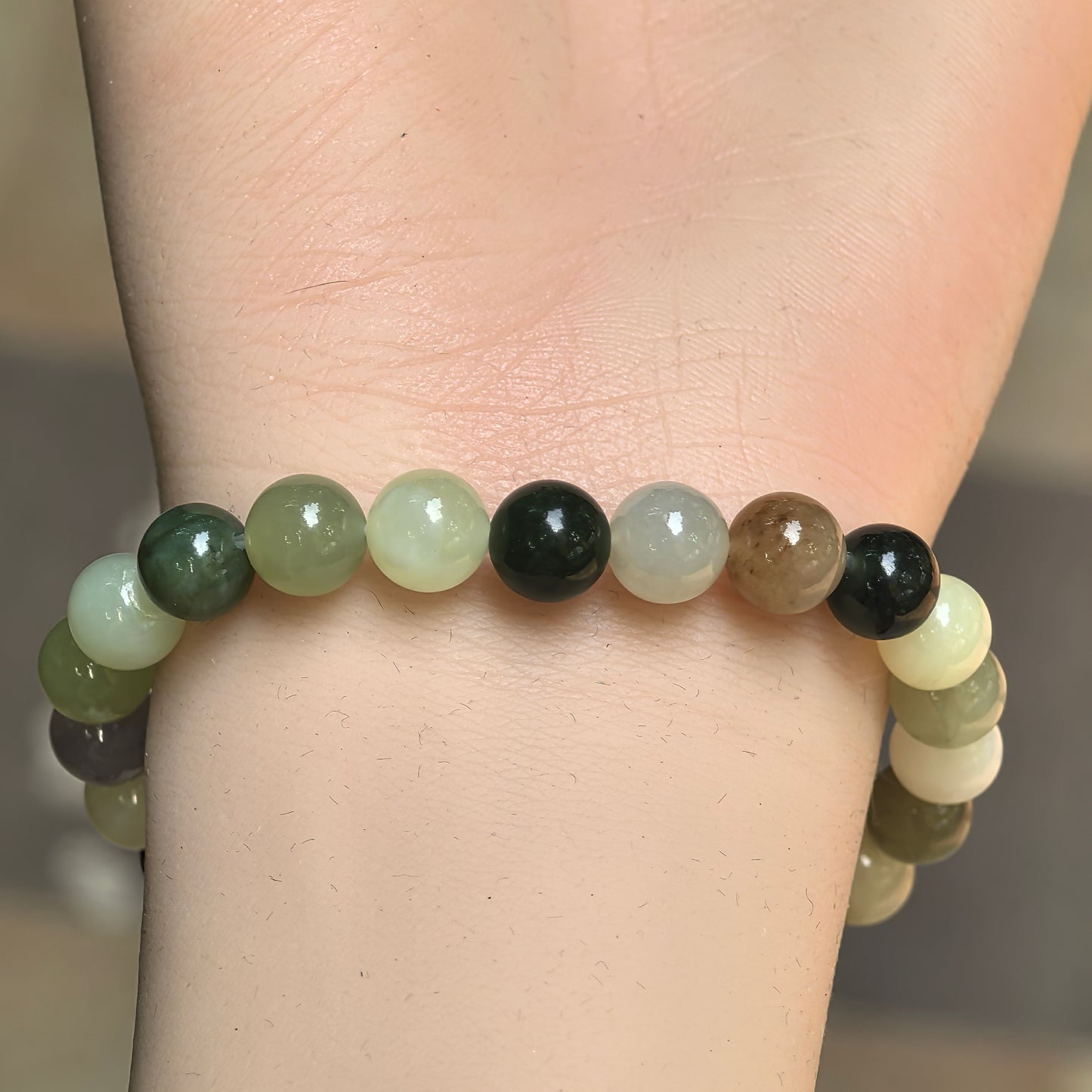 Natural Hetian jade bracelet displayed on stone with mixed green, creamy white, grayish lavender, and brown bead colors.
