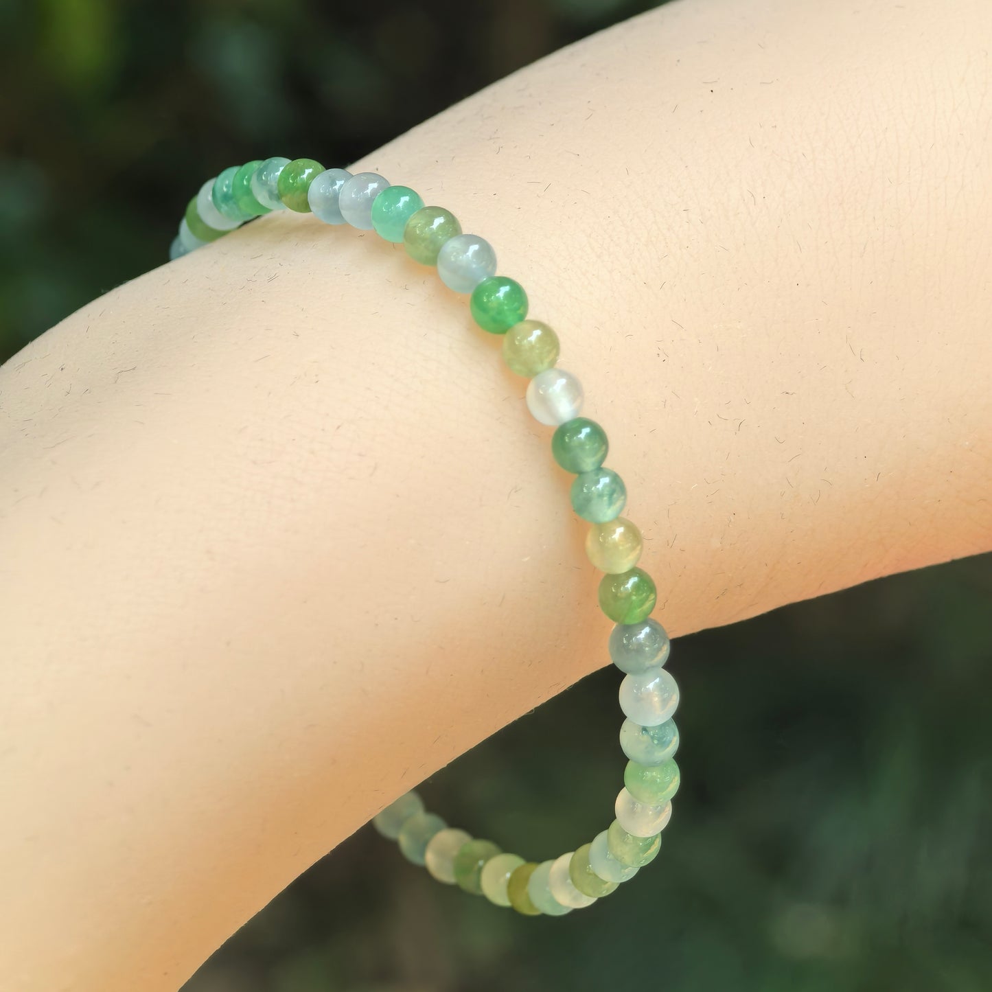 Natural Grade-A icy green multicolor jadeite bead bracelet worn on wrist with small glossy round beads.
