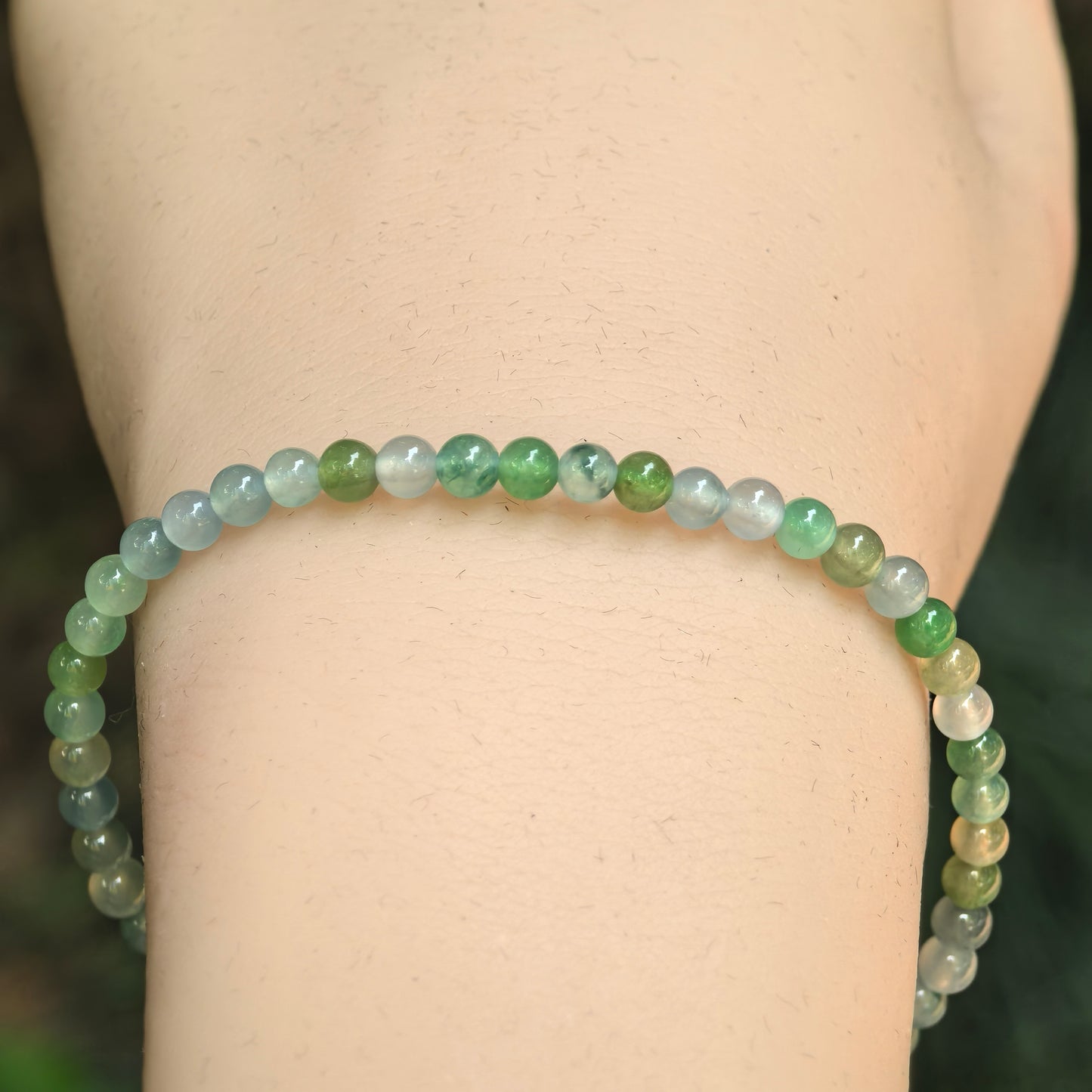 Close-up of icy jadeite bead bracelet showing green, blue-green, and white natural color variation.
