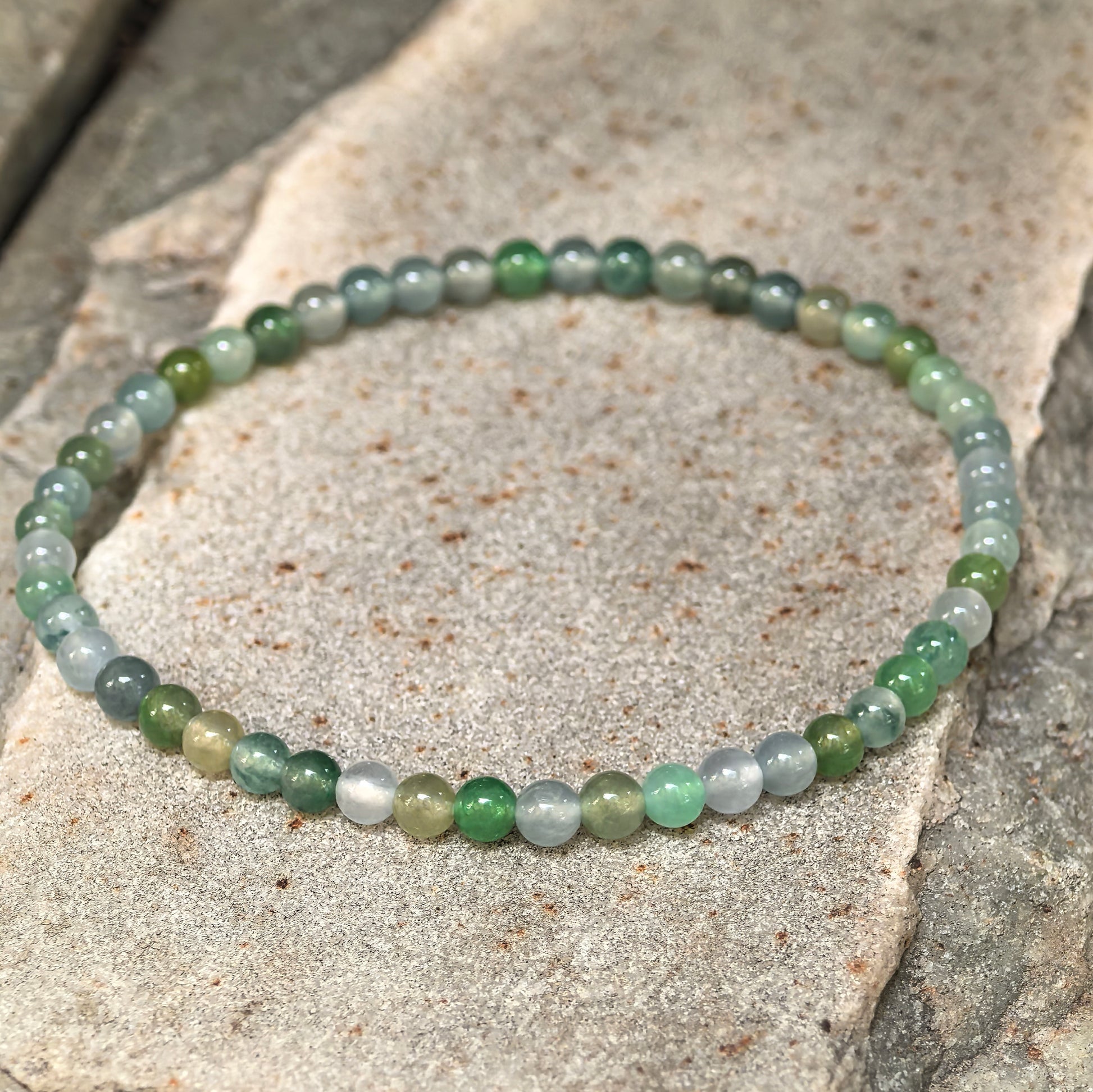 Icy green jadeite bead bracelet displayed from an angled view showing polished bead texture.
