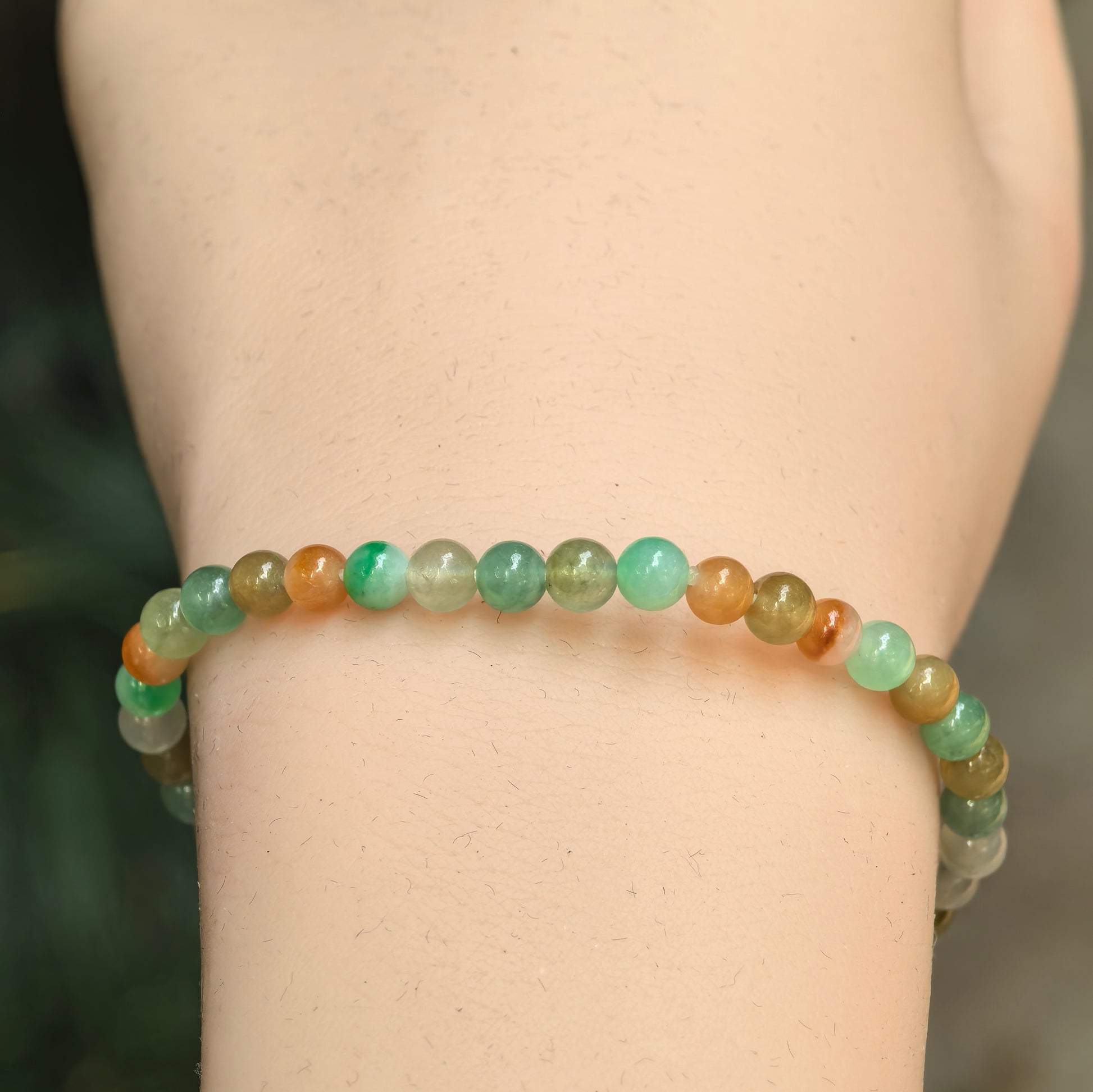 Close-up of multicolor jadeite bracelet with light green, brownish yellow, and white round beads.
