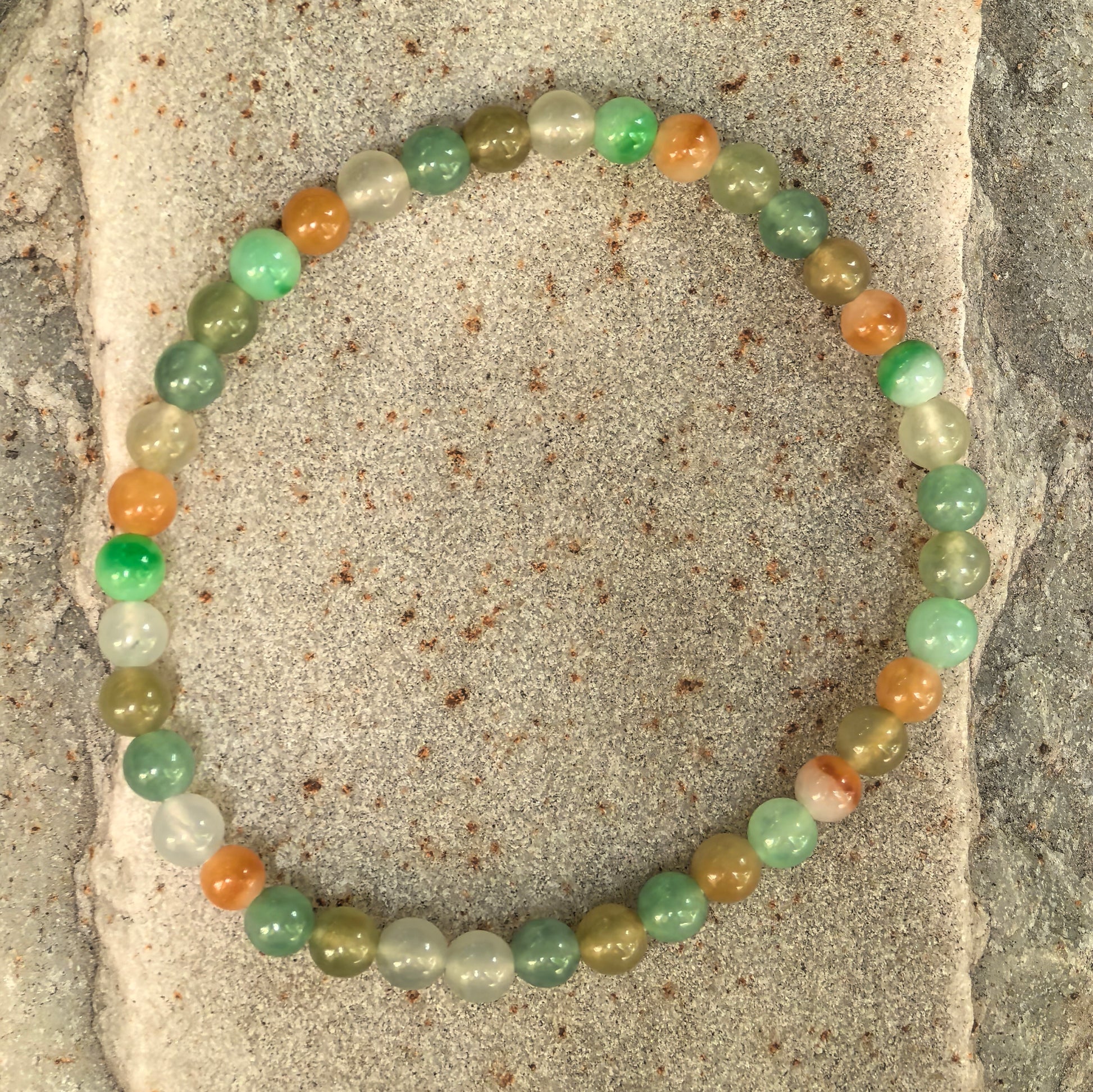 Natural Burmese jadeite bead bracelet displayed flat on a stone surface.

