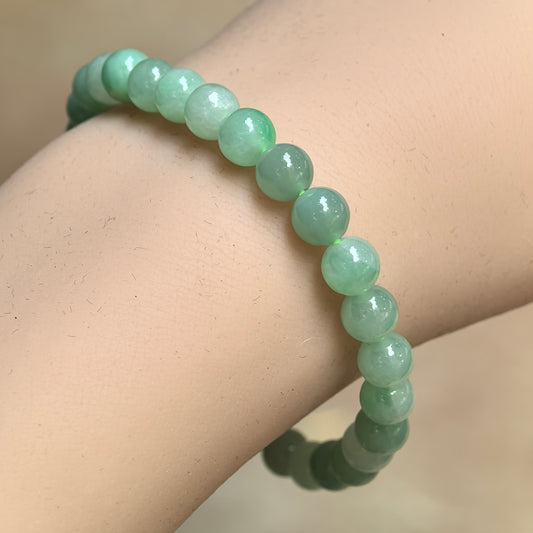 Natural Grade-A glutinous light green jadeite bead bracelet worn on wrist with glossy round beads.
