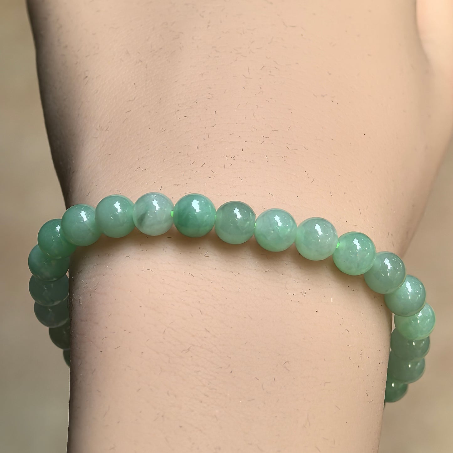 Close-up of light green jadeite bead bracelet showing natural green variations and polished surface.