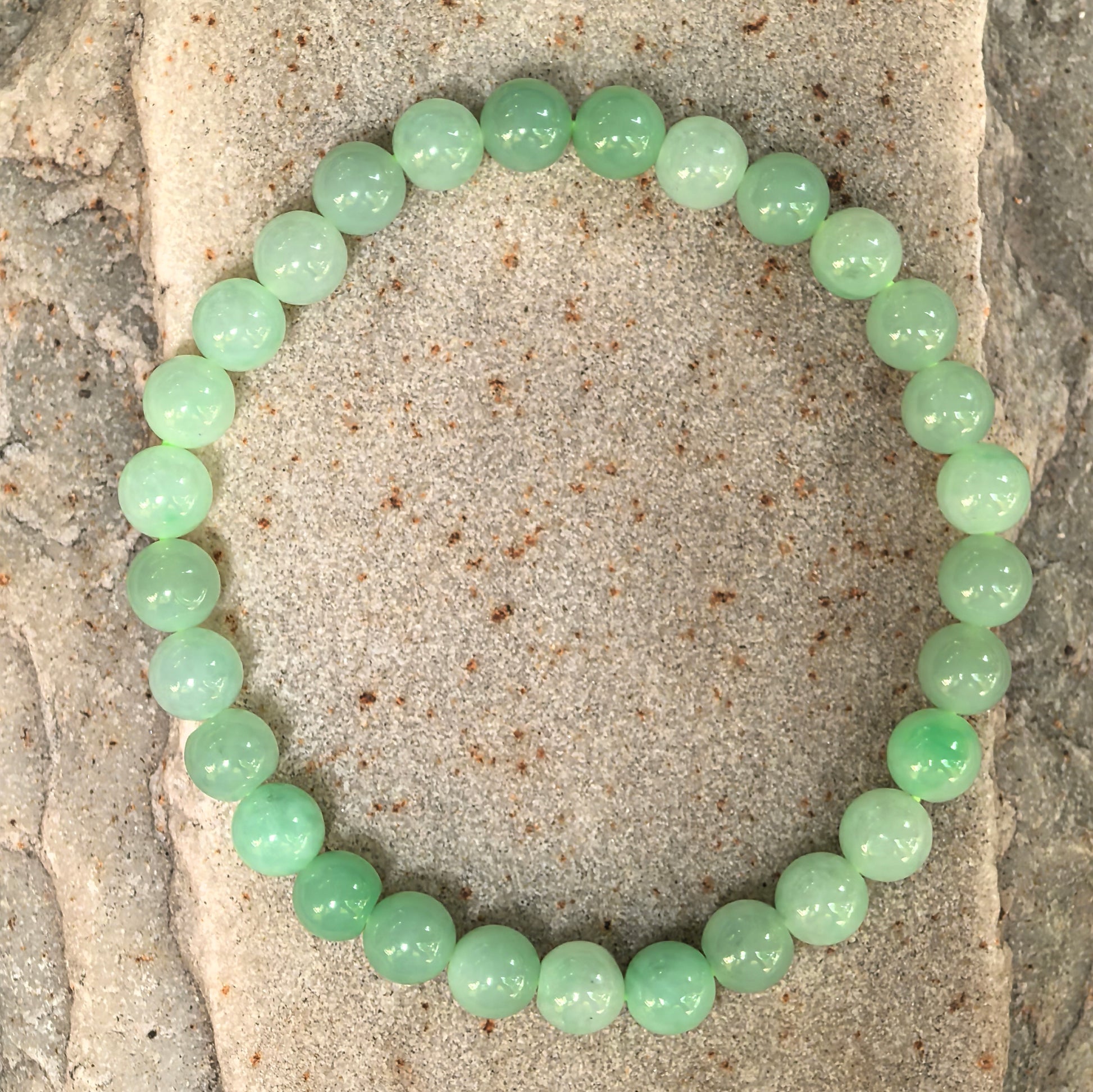 Glutinous light green round-bead jadeite bracelet laid flat on stone background.
