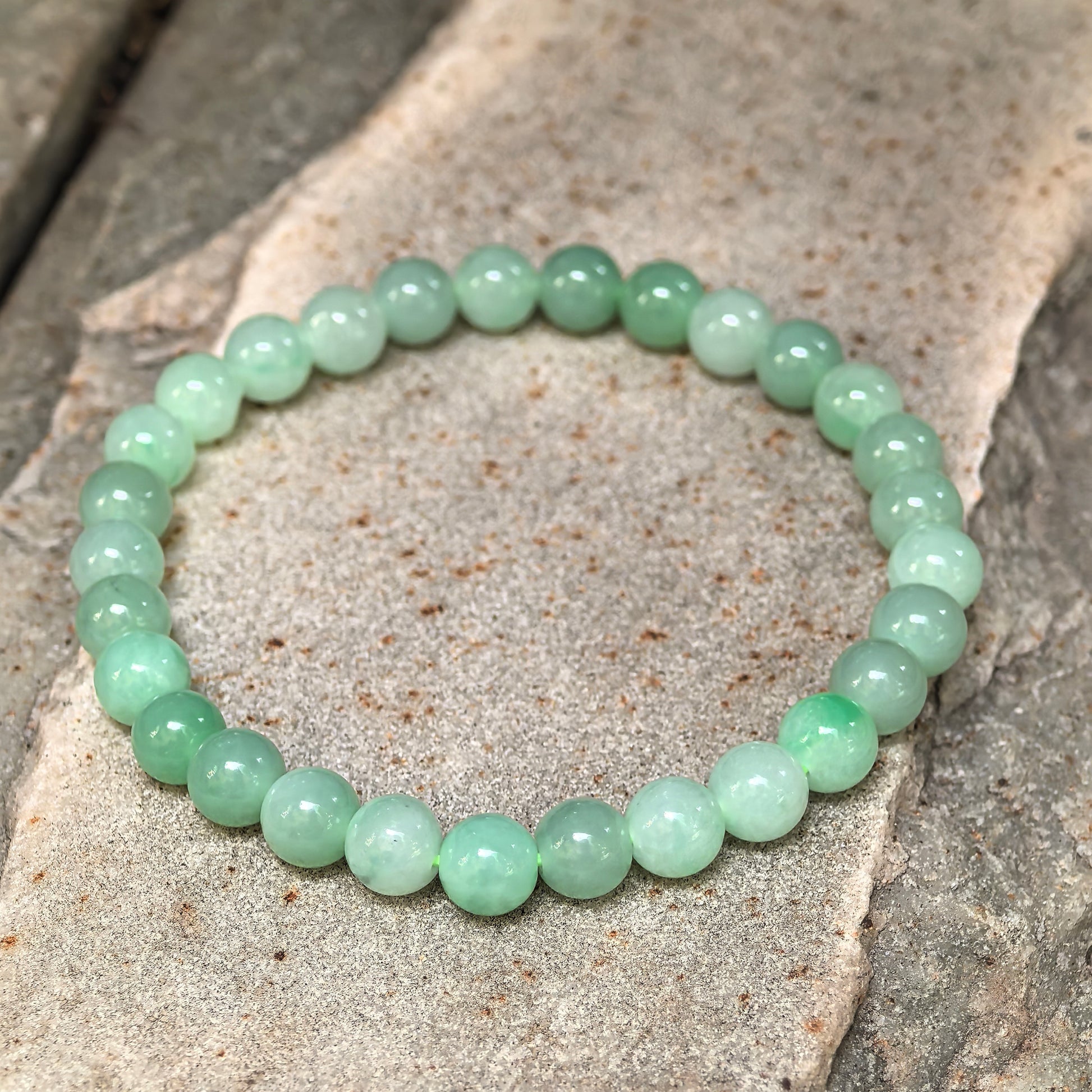 Natural Grade-A light green jadeite bracelet with 29 round beads shown from an angled view.
