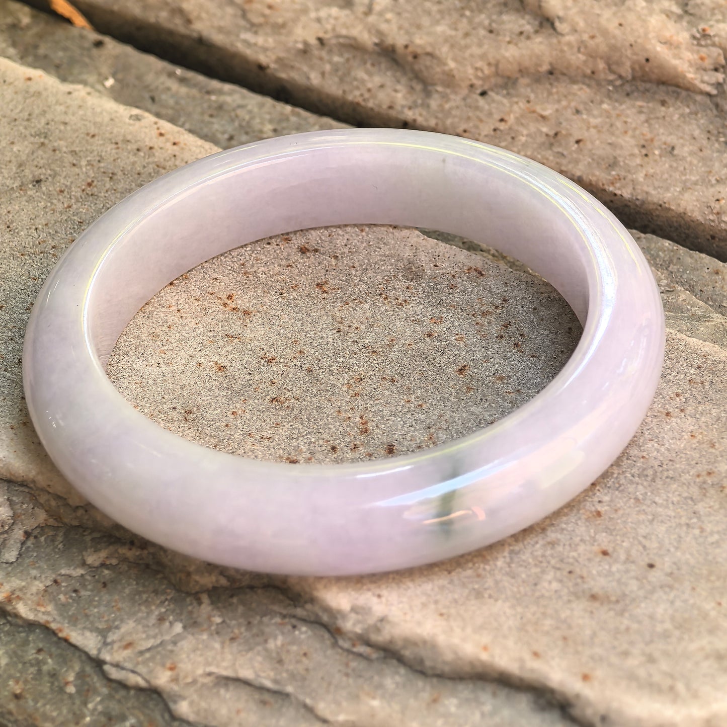 Natural Grade-A pale lavender Burmese jadeite bangle shown on stone background with rounded D-shape profile.
