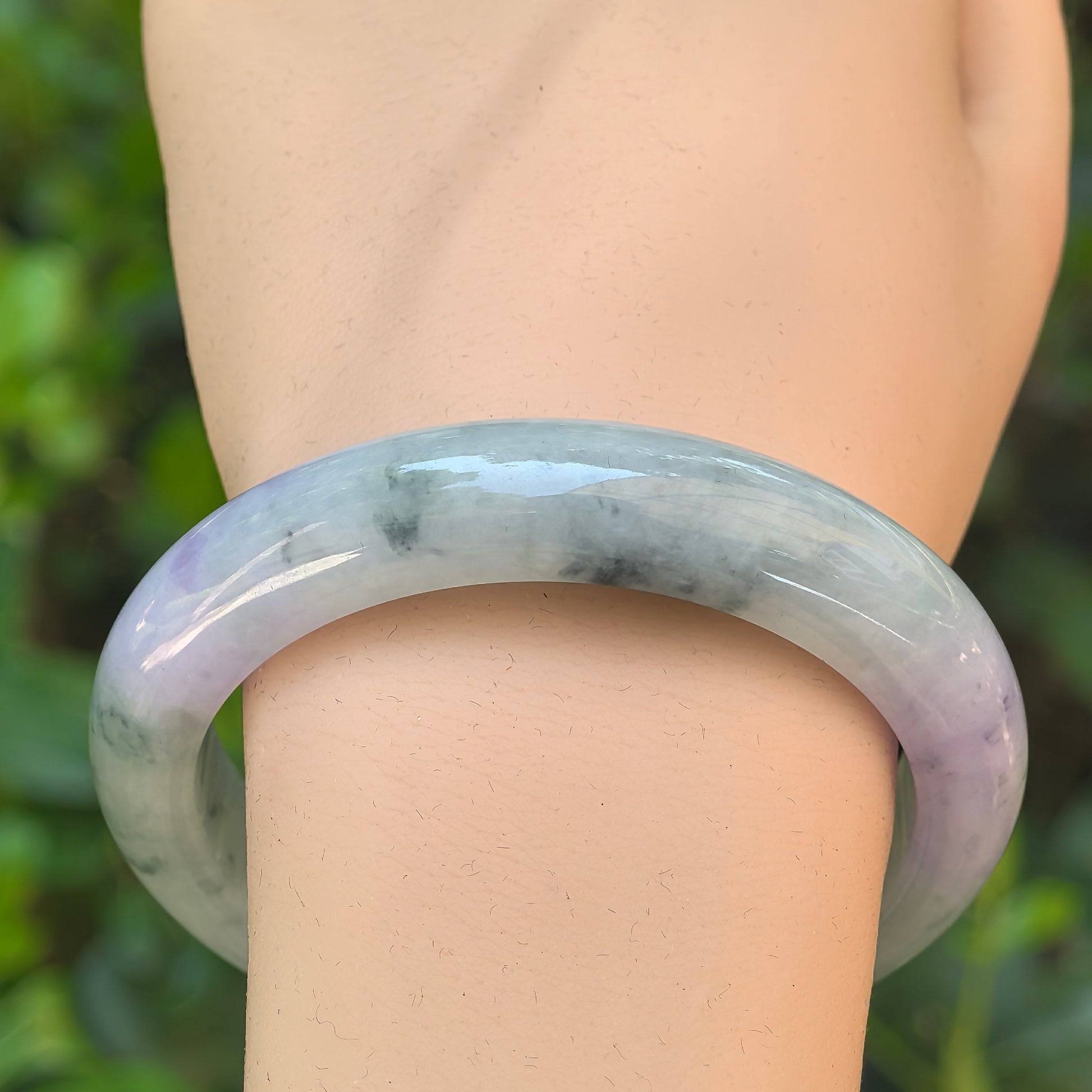 Close-up of lavender and pale green jadeite bangle showing dark green floral patterns and glossy surface.