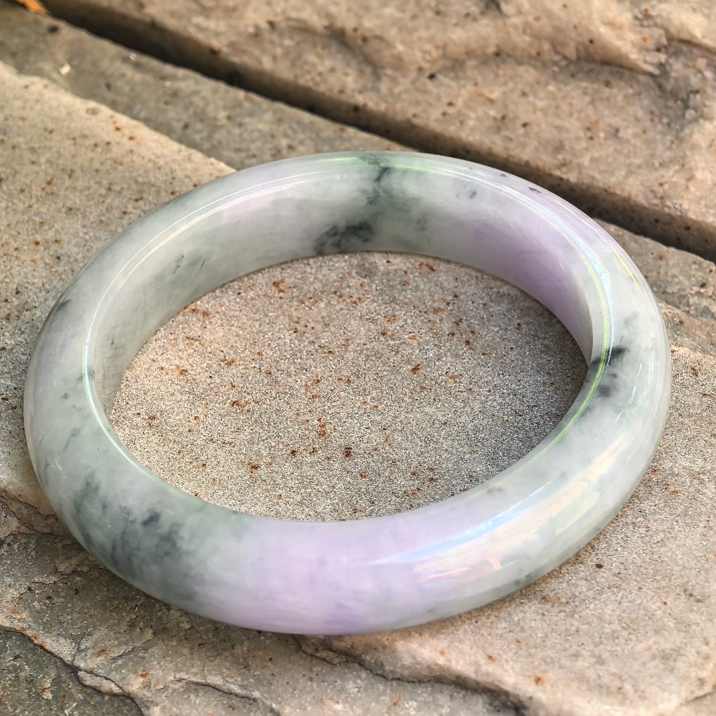 Natural jadeite D-shape bangle with light lavender tone, pale green areas, and visible mineral inclusions.