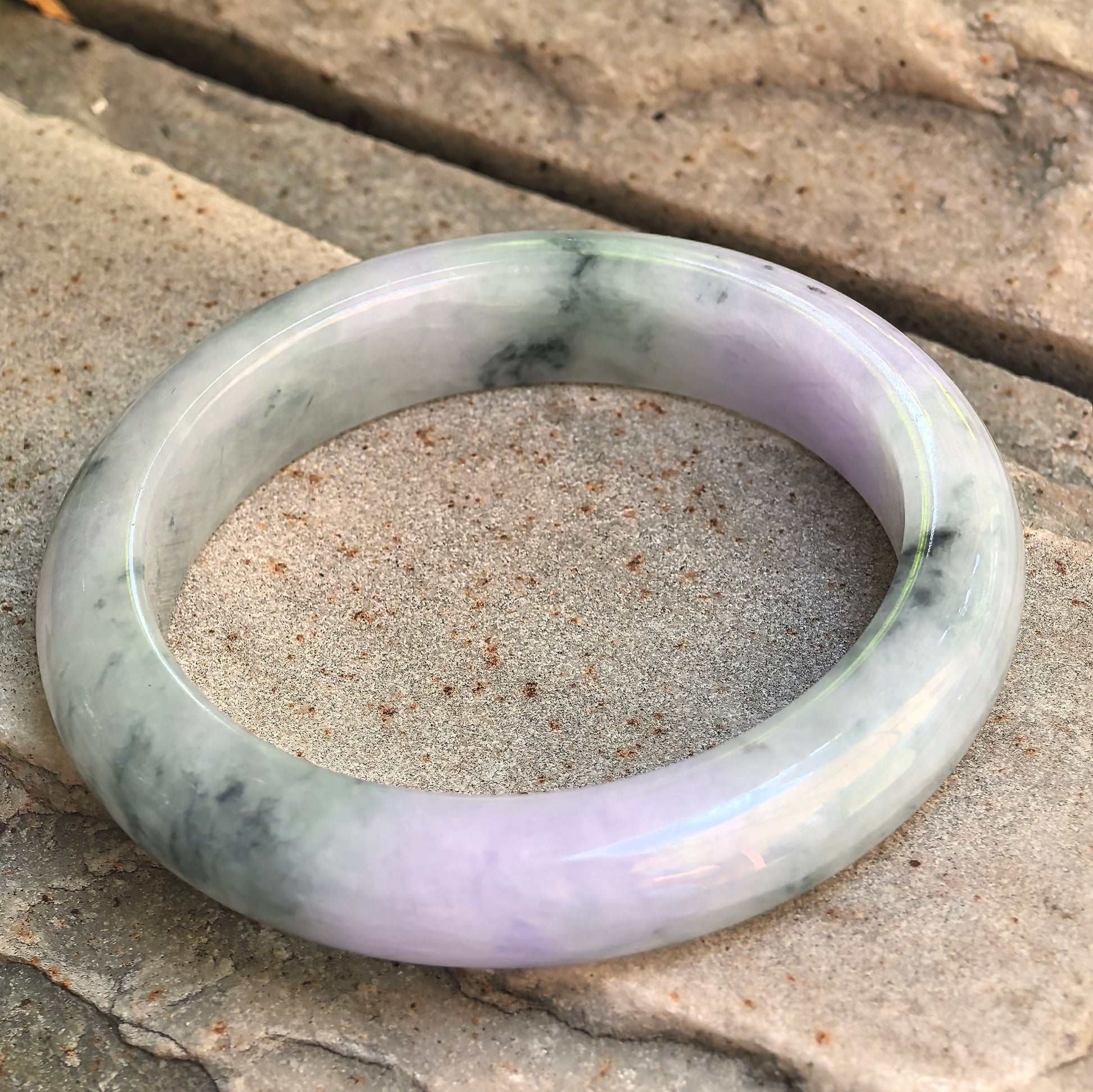 Natural jadeite D-shape bangle with light lavender tone, pale green areas, and visible mineral inclusions.