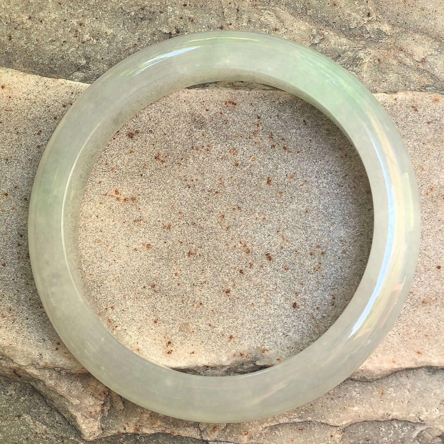 Icy glutinous light green Burmese jadeite bangle displayed on stone background with soft translucency.