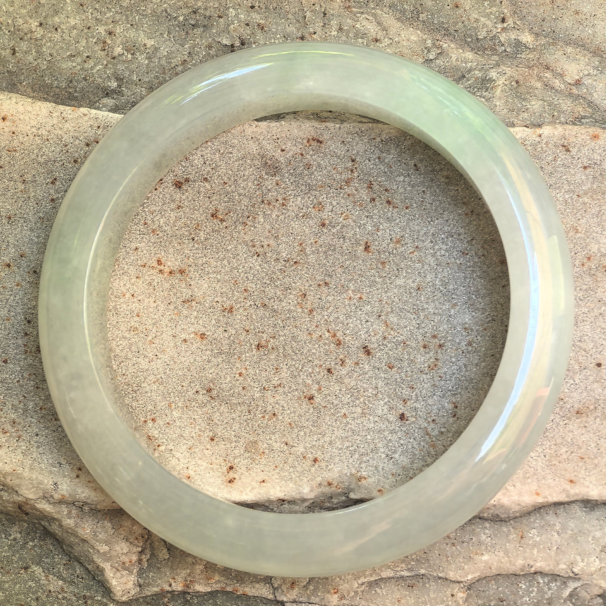 Icy glutinous light green Burmese jadeite bangle displayed on stone background with soft translucency.
