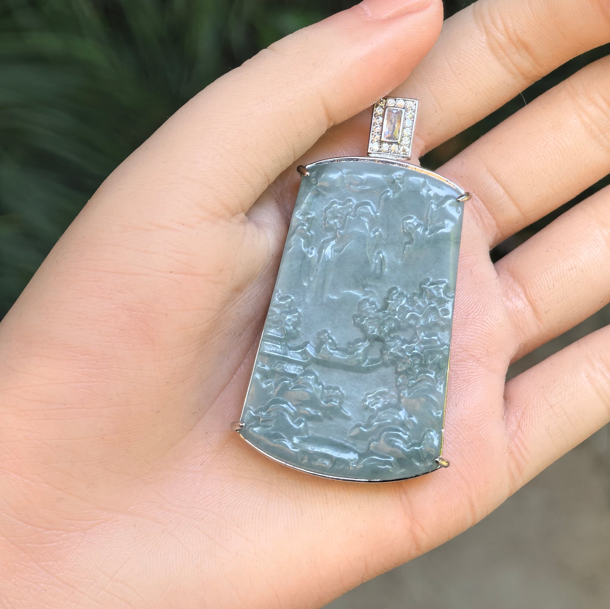 Teal blue landscape jadeite pendant held in hand, showing rectangular plaque shape and non-precious metal setting.