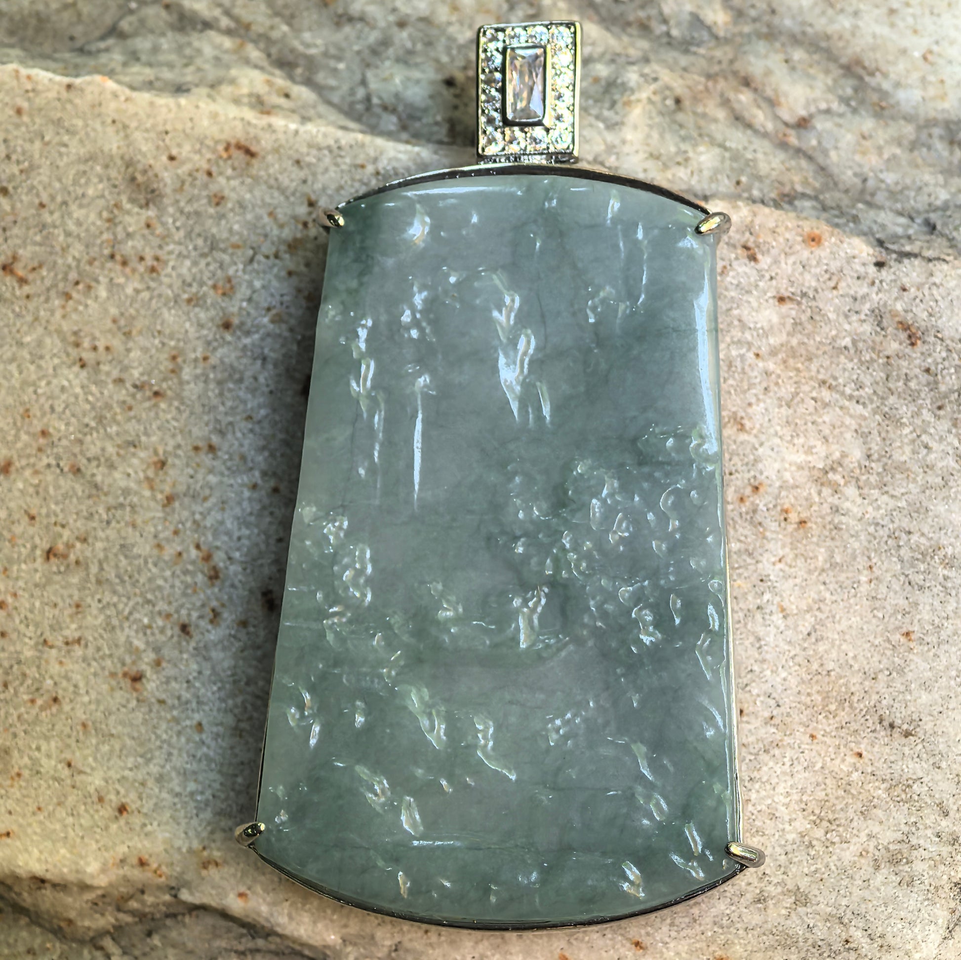 Close-up of carved Guatemalan jadeite landscape pendant showing mountain, water, tree, and pavilion details.
