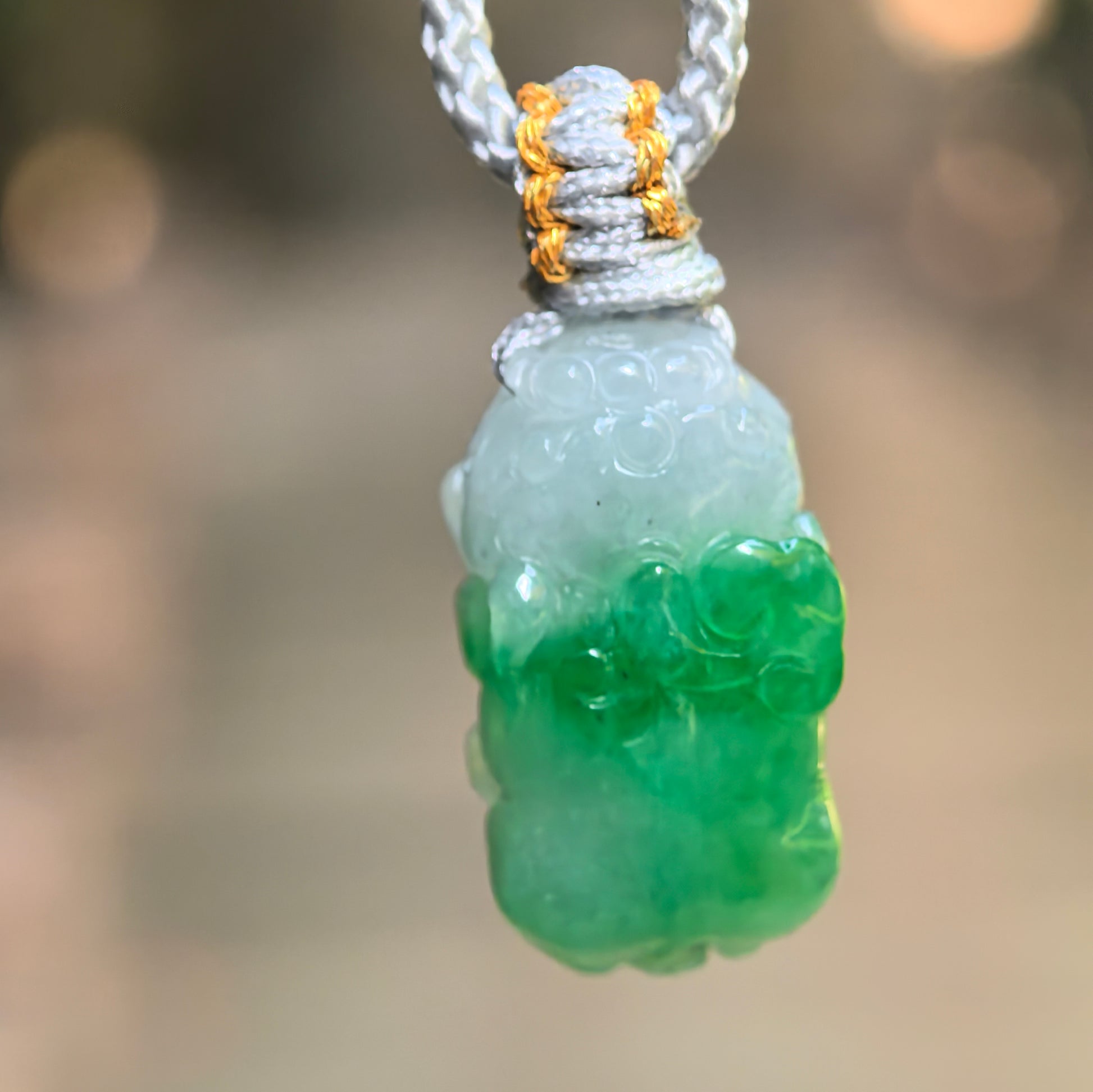 Natural Grade-A glutinous half-green Pixiu jadeite pendant hanging on gray cord with vivid green lower section.