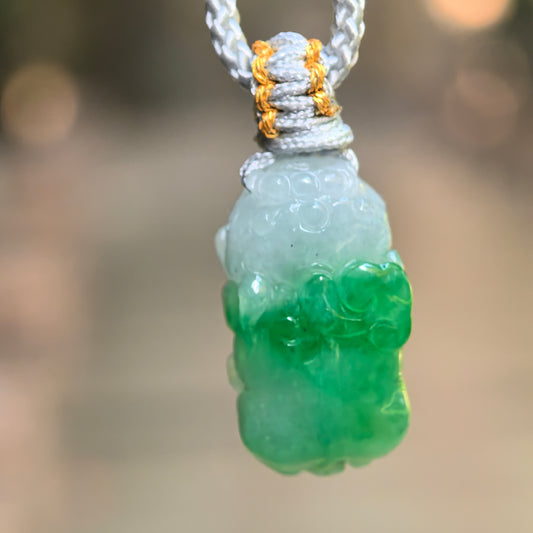 Natural Grade-A glutinous half-green Pixiu jadeite pendant hanging on gray cord with vivid green lower section.