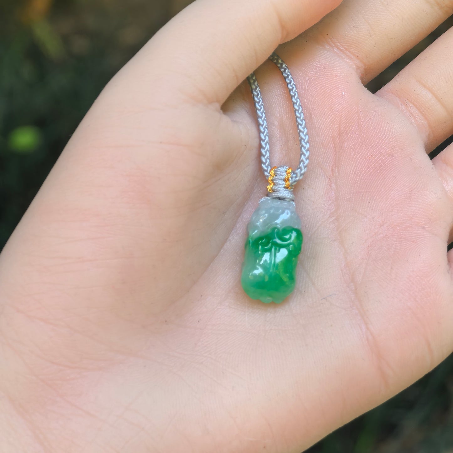 Small half-green Pixiu jadeite pendant shown on palm for size reference with cord attached.