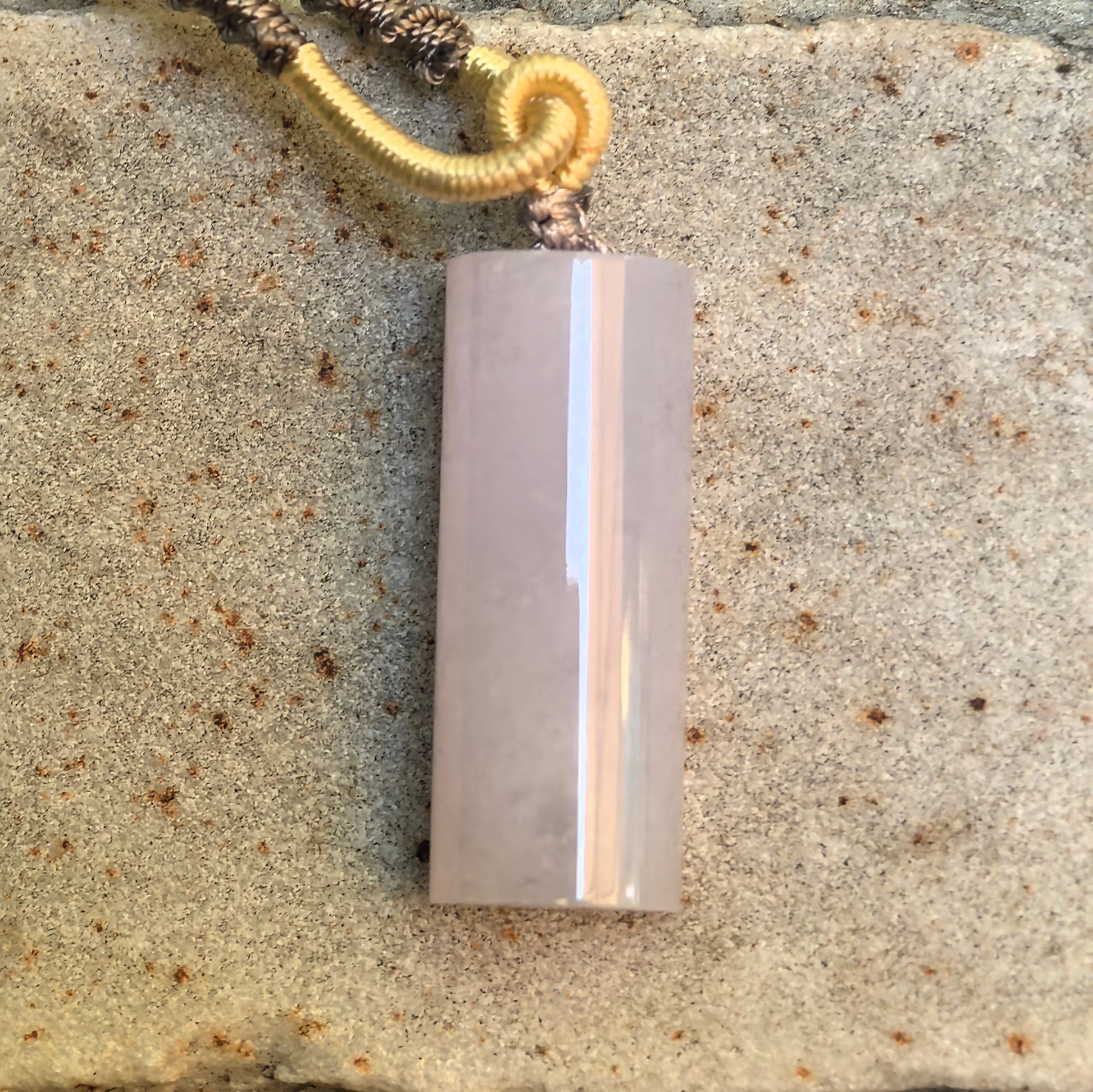 Light purple jadeite plain pillar pendant displayed on stone background with cord attached.
