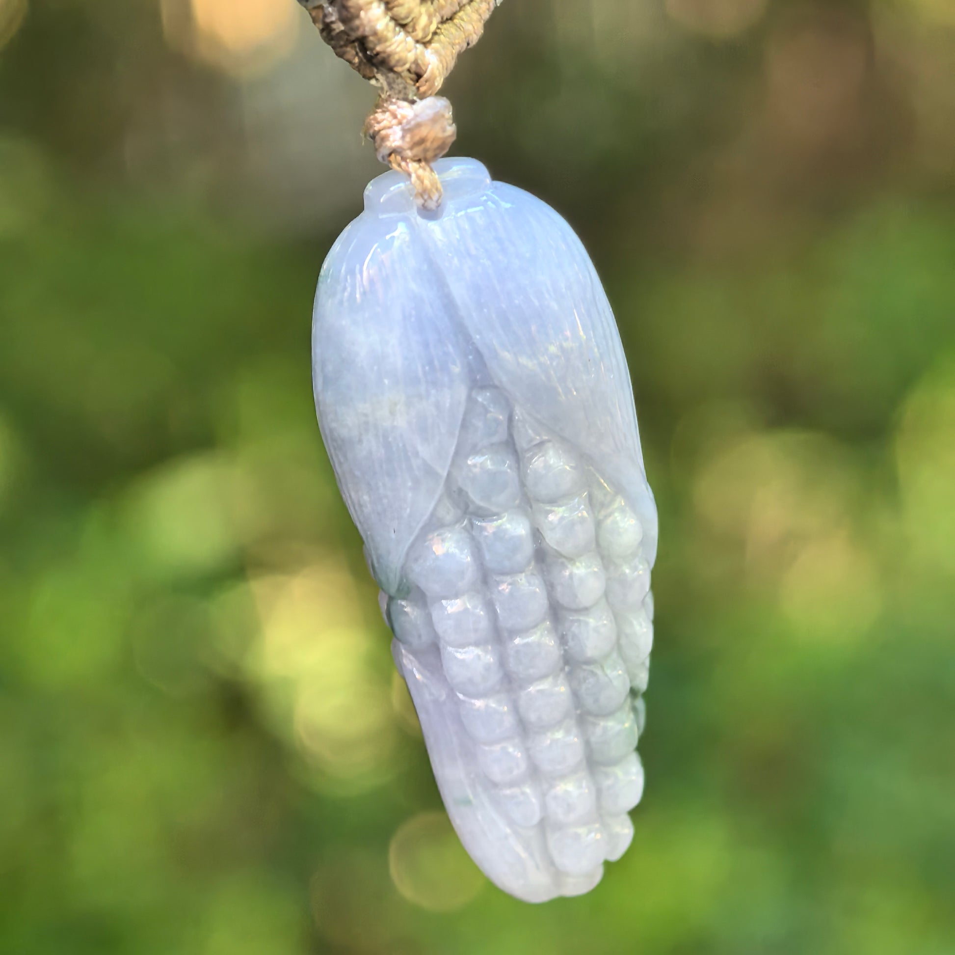 Close-up of light lavender-green corn jadeite pendant showing carved kernels and husk details.
