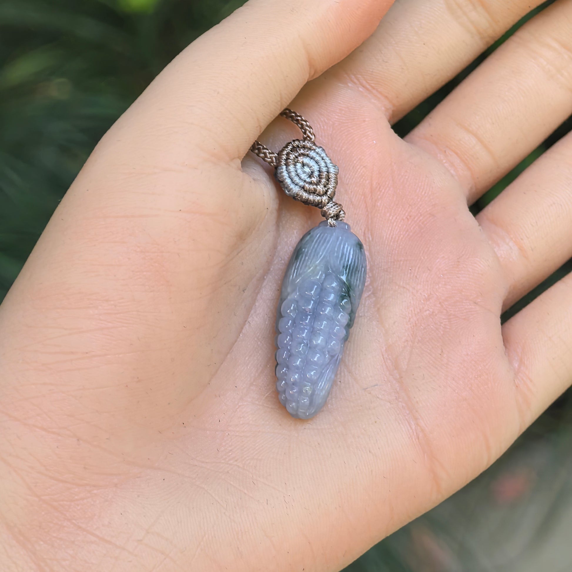 Glutinous lavender-green jadeite corn pendant shown in hand with soft natural luster.

