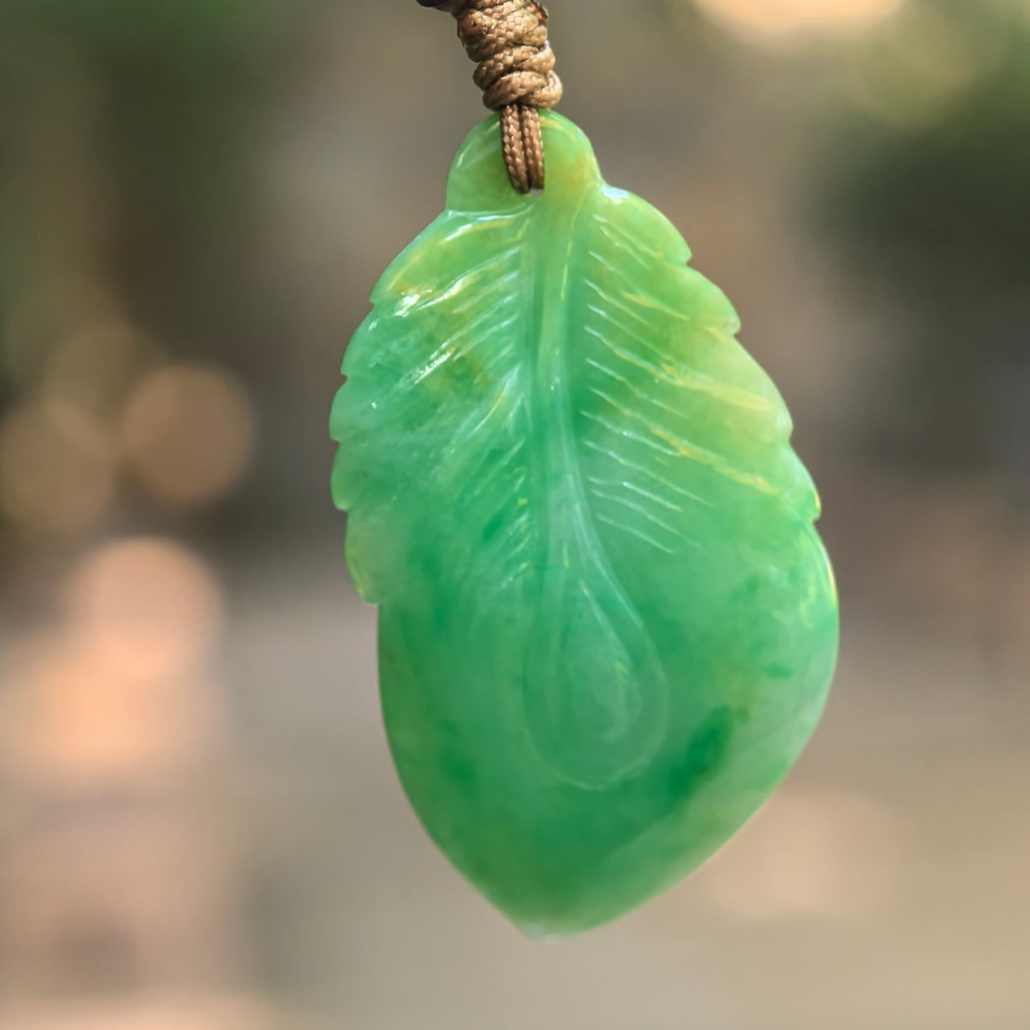Natural Grade-A glutinous green leaf jadeite pendant hanging on cord with soft green color variation.