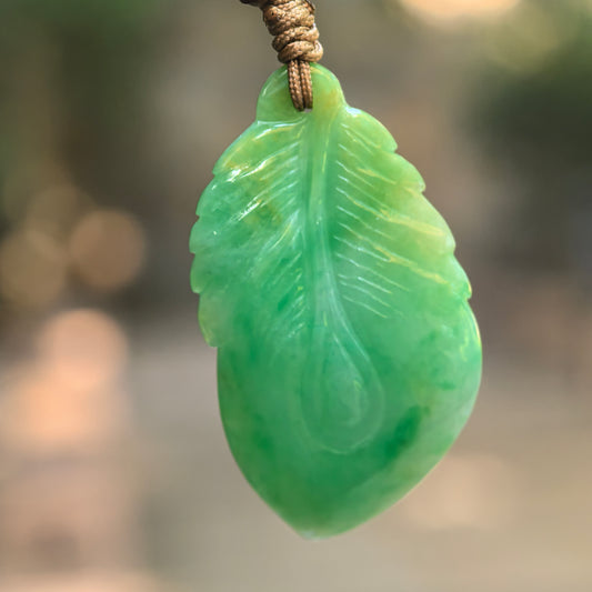 Natural Grade-A glutinous green leaf jadeite pendant hanging on cord with soft green color variation.