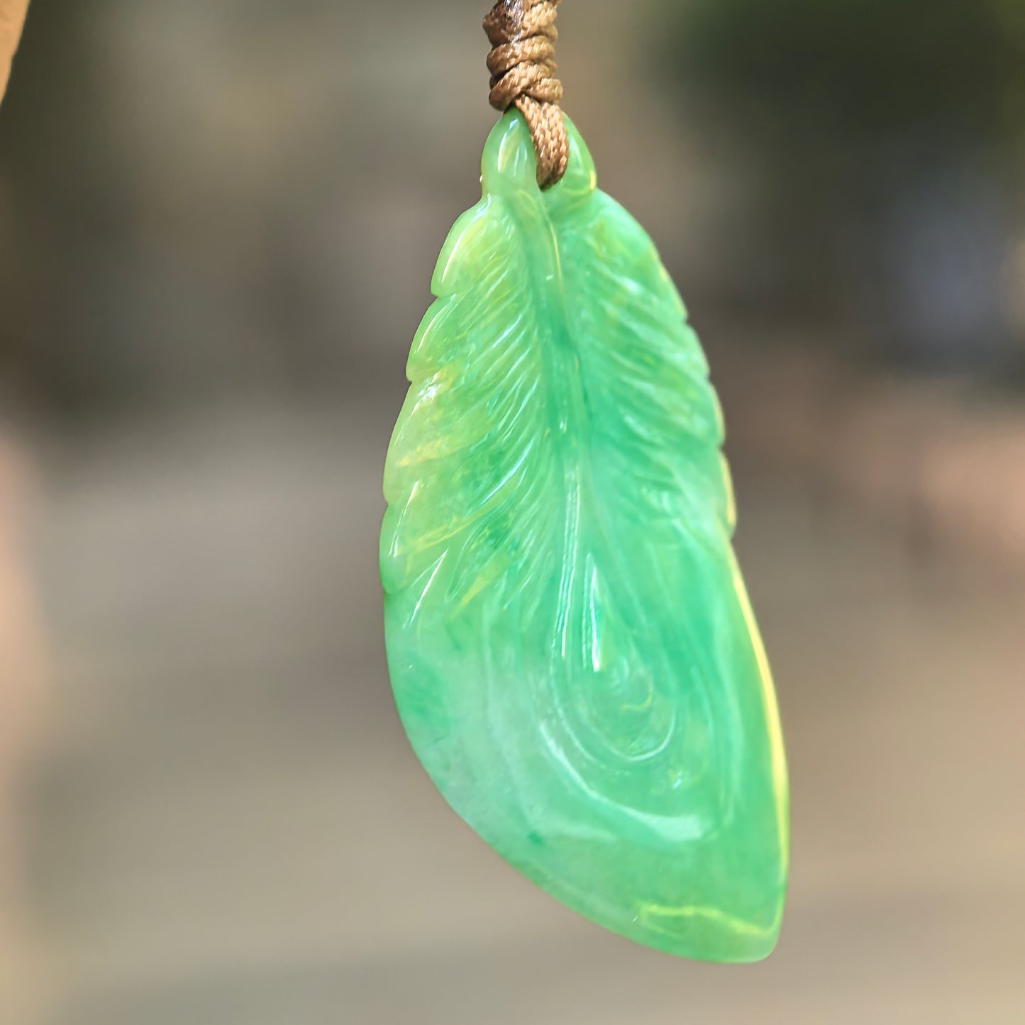 Close-up side view of green leaf jadeite pendant showing carved leaf veins and smooth polished texture.