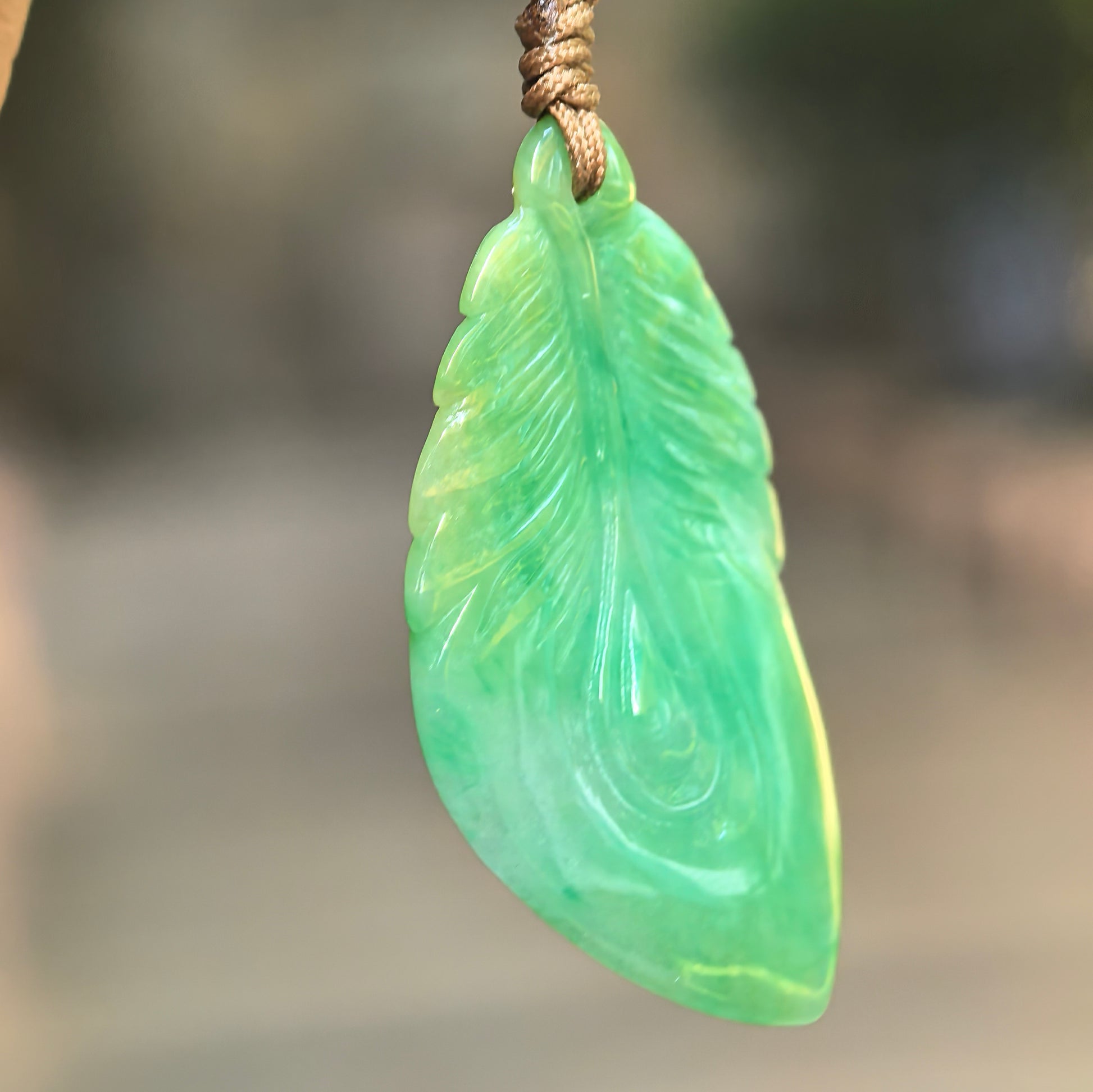 Close-up side view of green leaf jadeite pendant showing carved leaf veins and smooth polished texture.