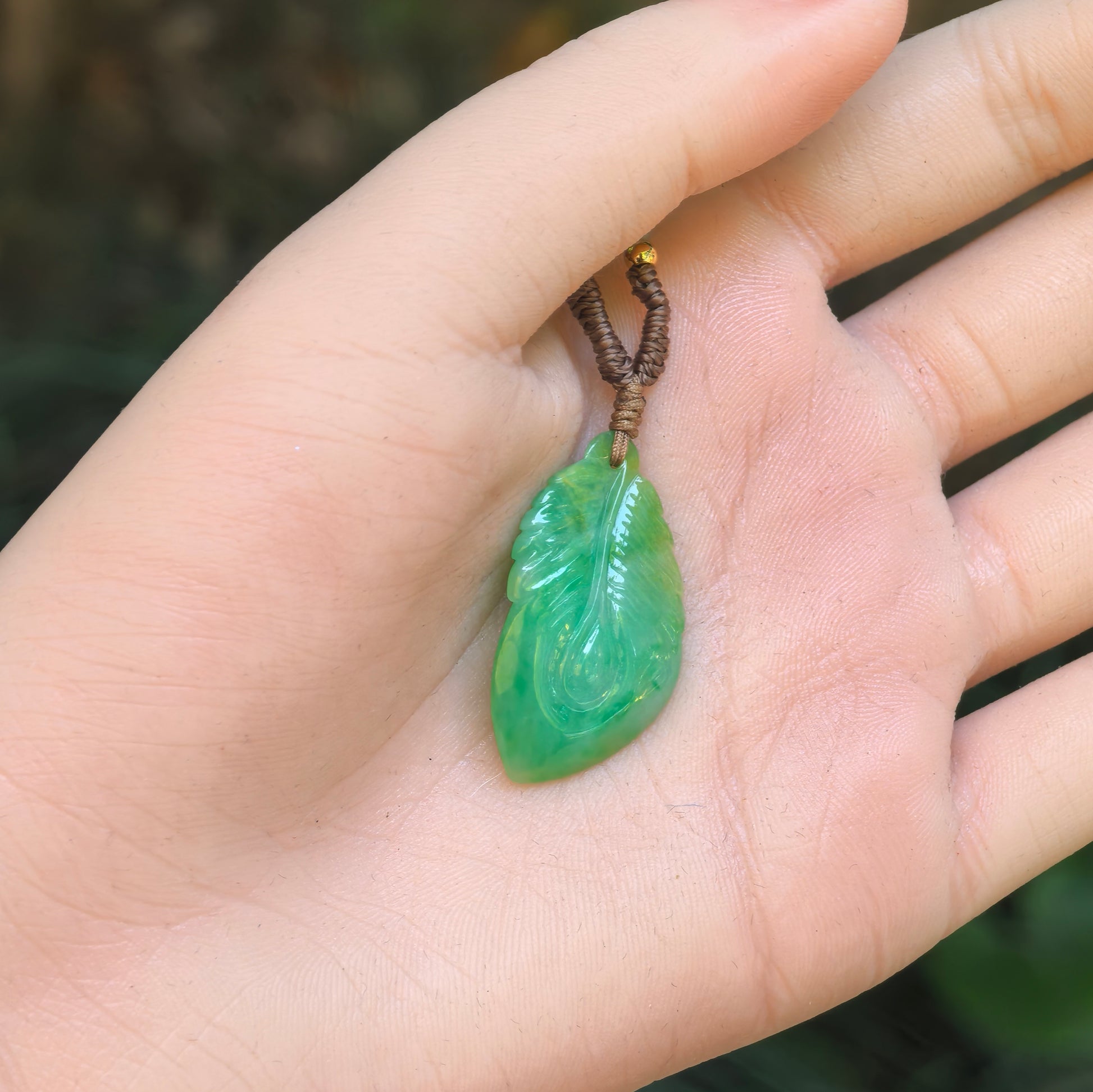 Natural Grade-A green leaf jadeite pendant shown on palm for size reference.
