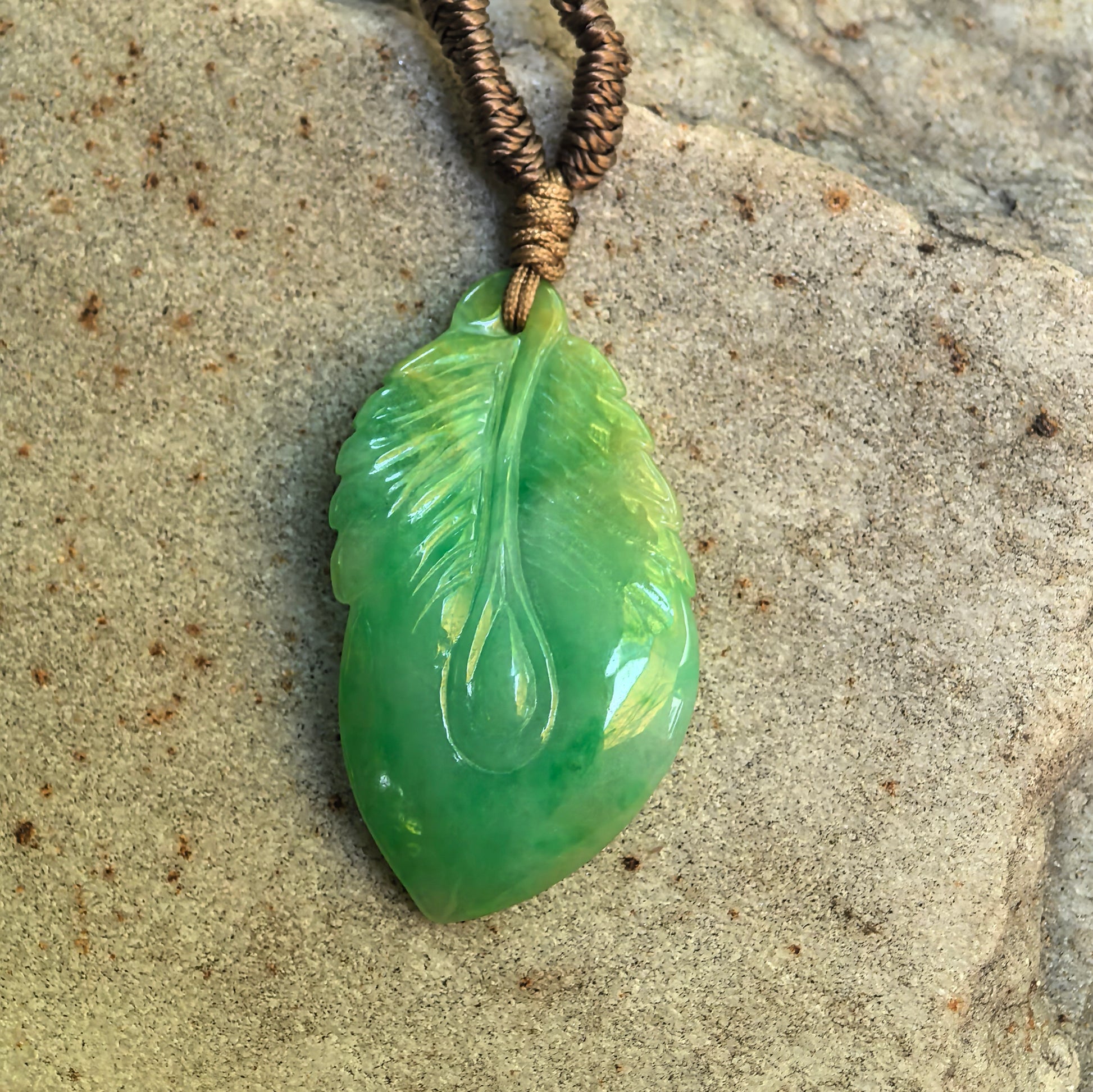 Glutinous green jadeite leaf pendant displayed on stone surface with natural light reflection.
